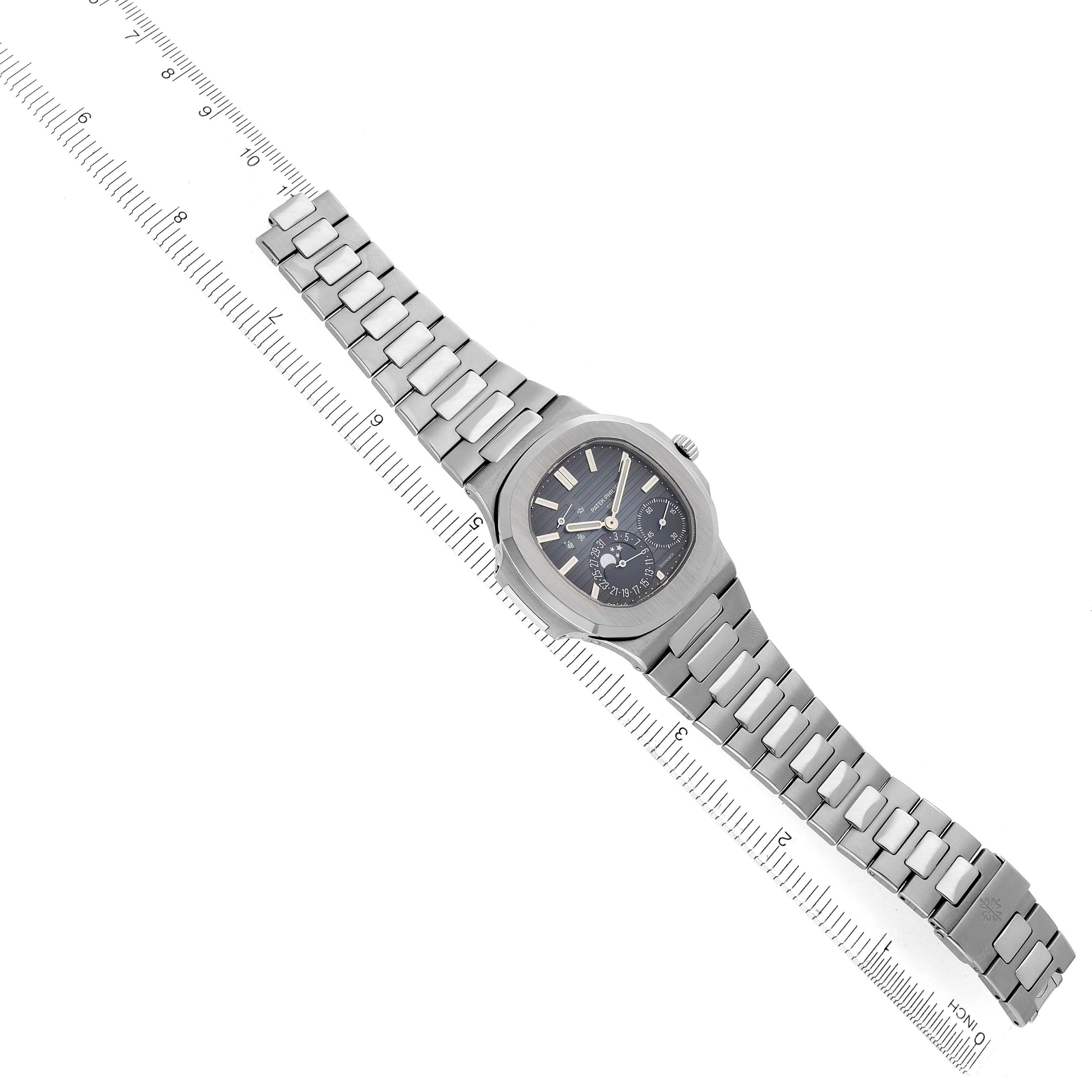 The Patek Philippe Nautilus 5712/1A-001 Men's Stainless Steel Blue Dial watch is shown at an angled view, highlighting the face, bracelet, and side profile alongside a ruler for scale.
