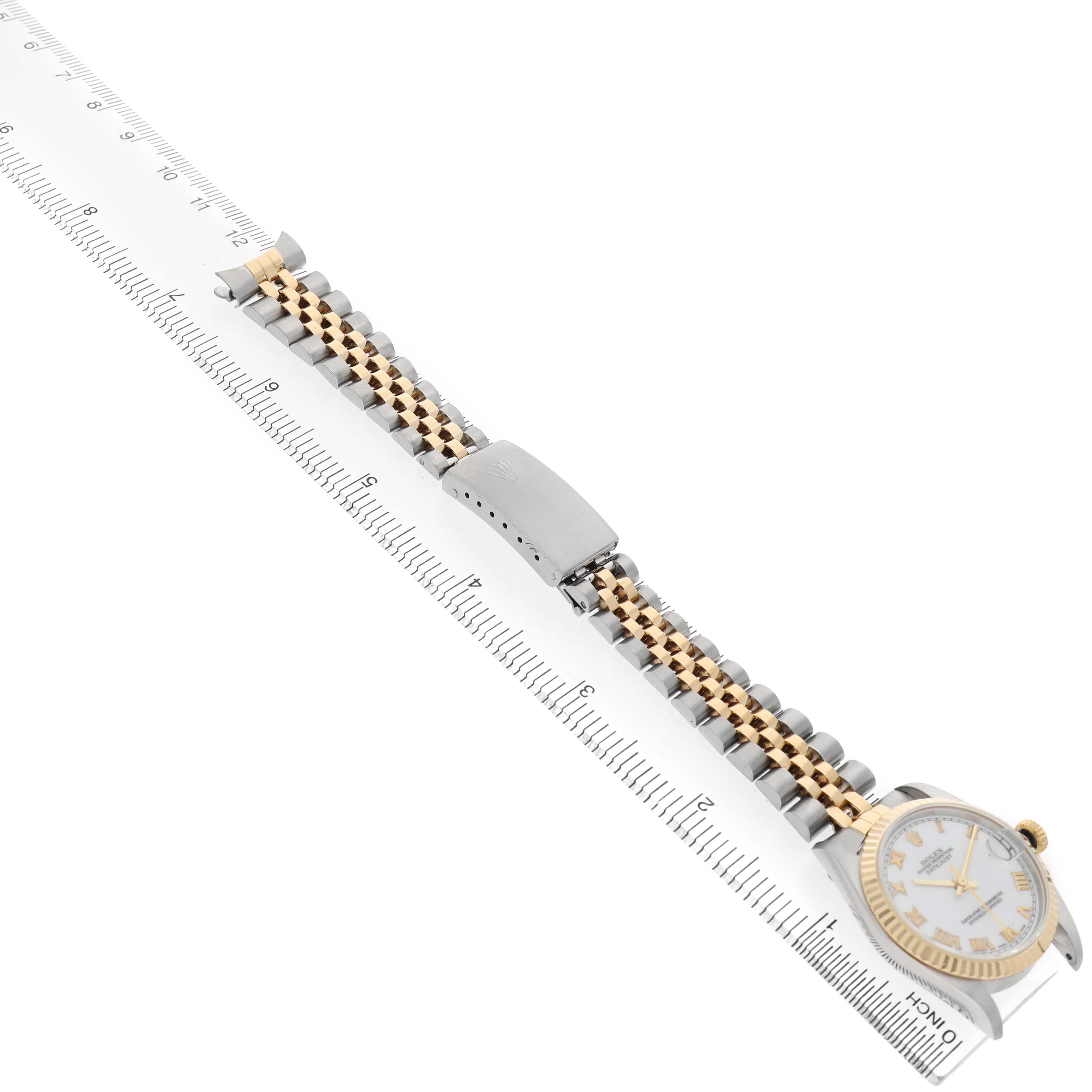 The Rolex Mid-Size 78273 Women's Steel and Gold (two tone) White Dial watch is shown lying flat on a ruler, displaying its bracelet, clasp, and partially visible face.