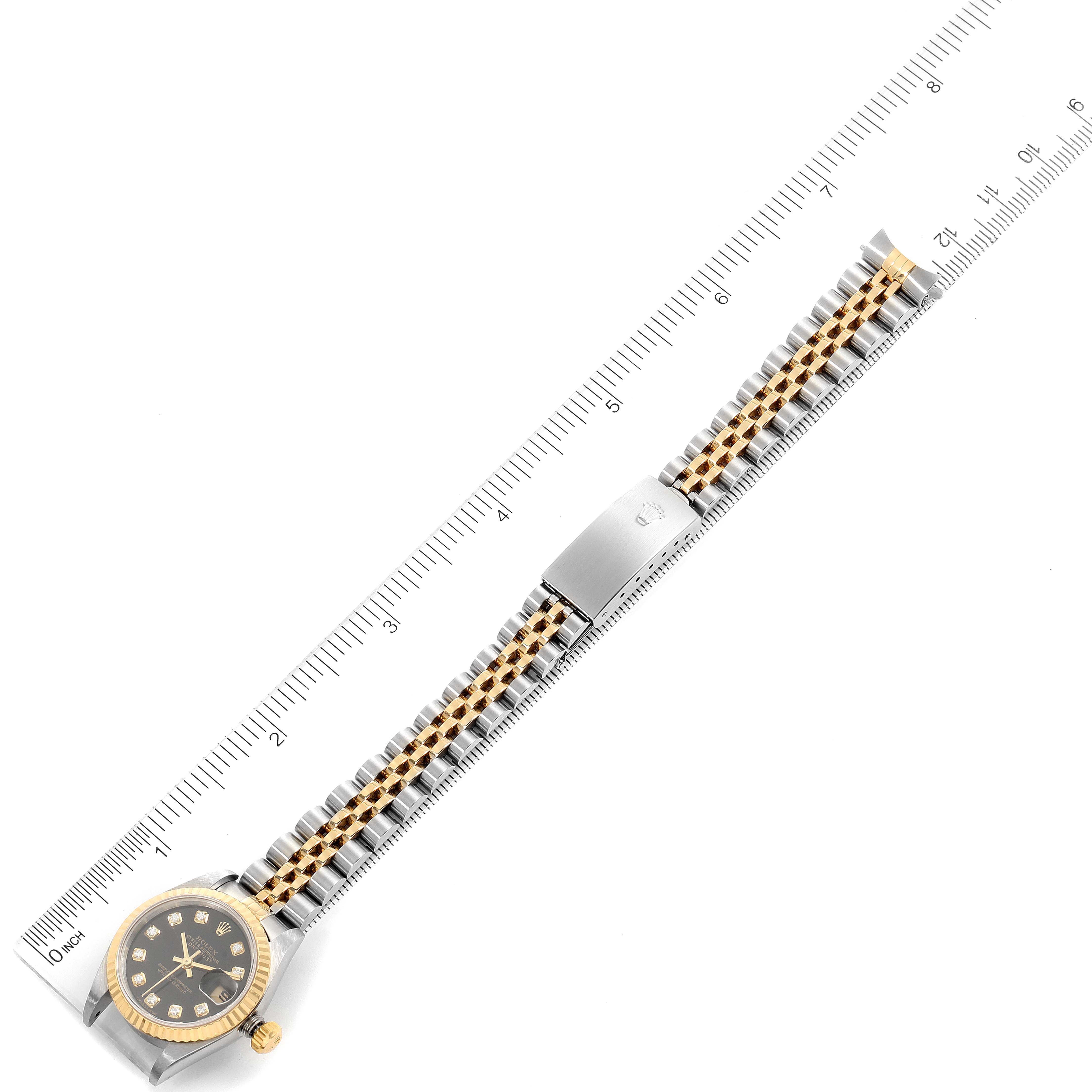 This image shows a Rolex Datejust 79173 Women's Steel and Gold (two tone) Black Dial 79173 Women's Steel and Gold (two tone) Black Dial watch laid flat with a ruler measuring its length, displaying the face, bezel, bracelet, and clasp.