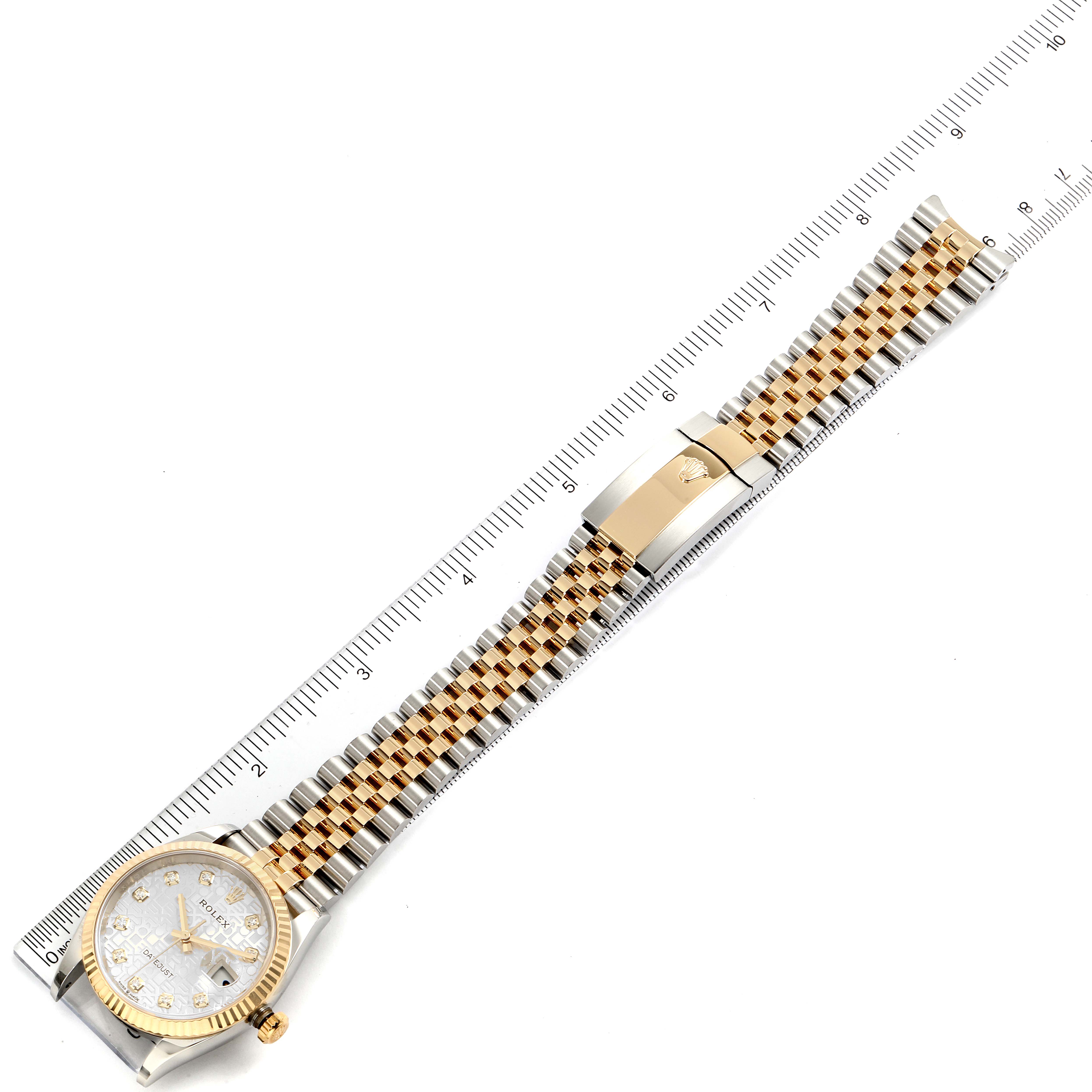 The Datejust by Rolex is viewed from above, showing the face, band, and clasp, aligned with a measuring ruler.