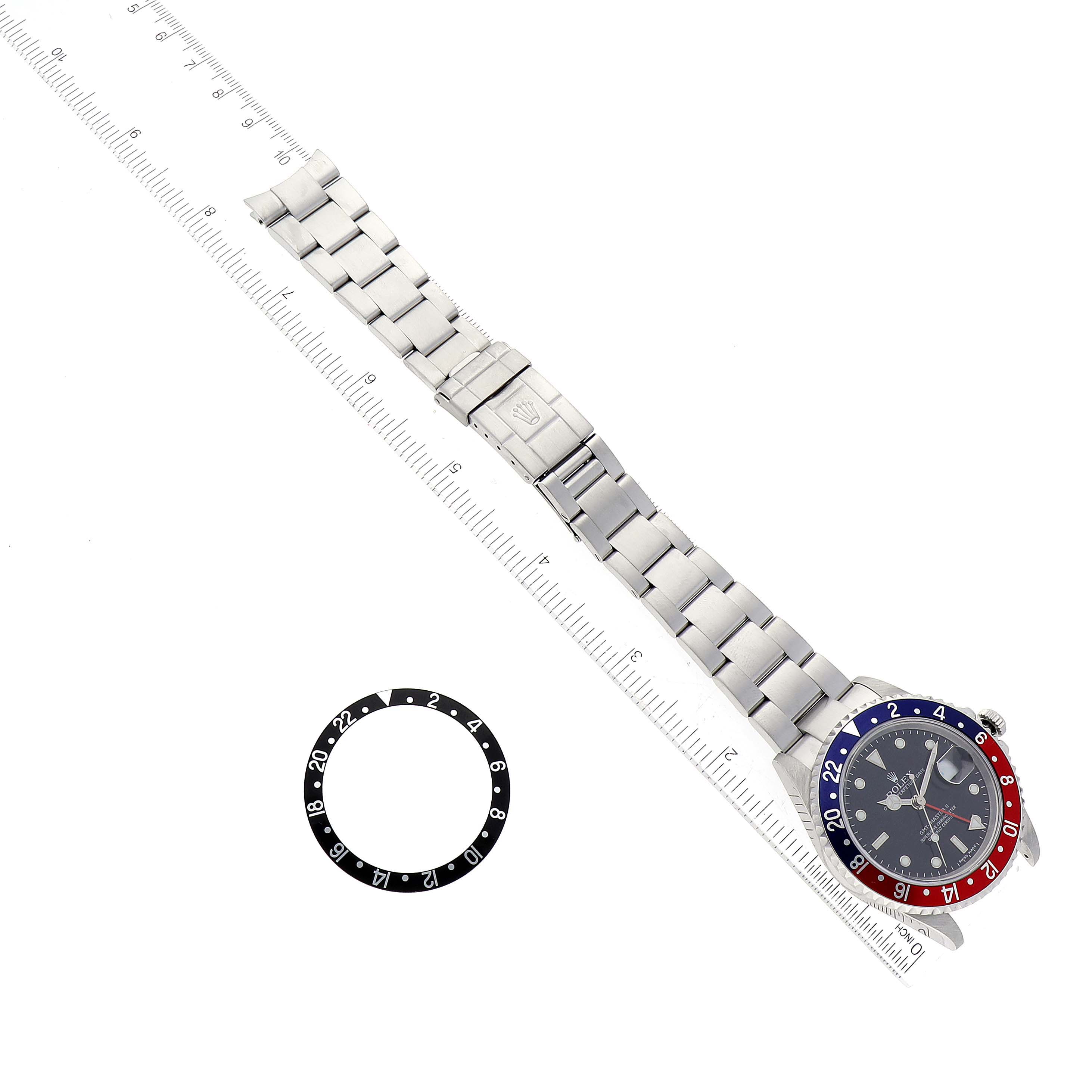 The image shows the front view of a Rolex GMT-Master 16710 Men's Stainless Steel Black Dial 16710 Men's Stainless Steel Black Dial watch and an additional bezel insert, placed next to a ruler.