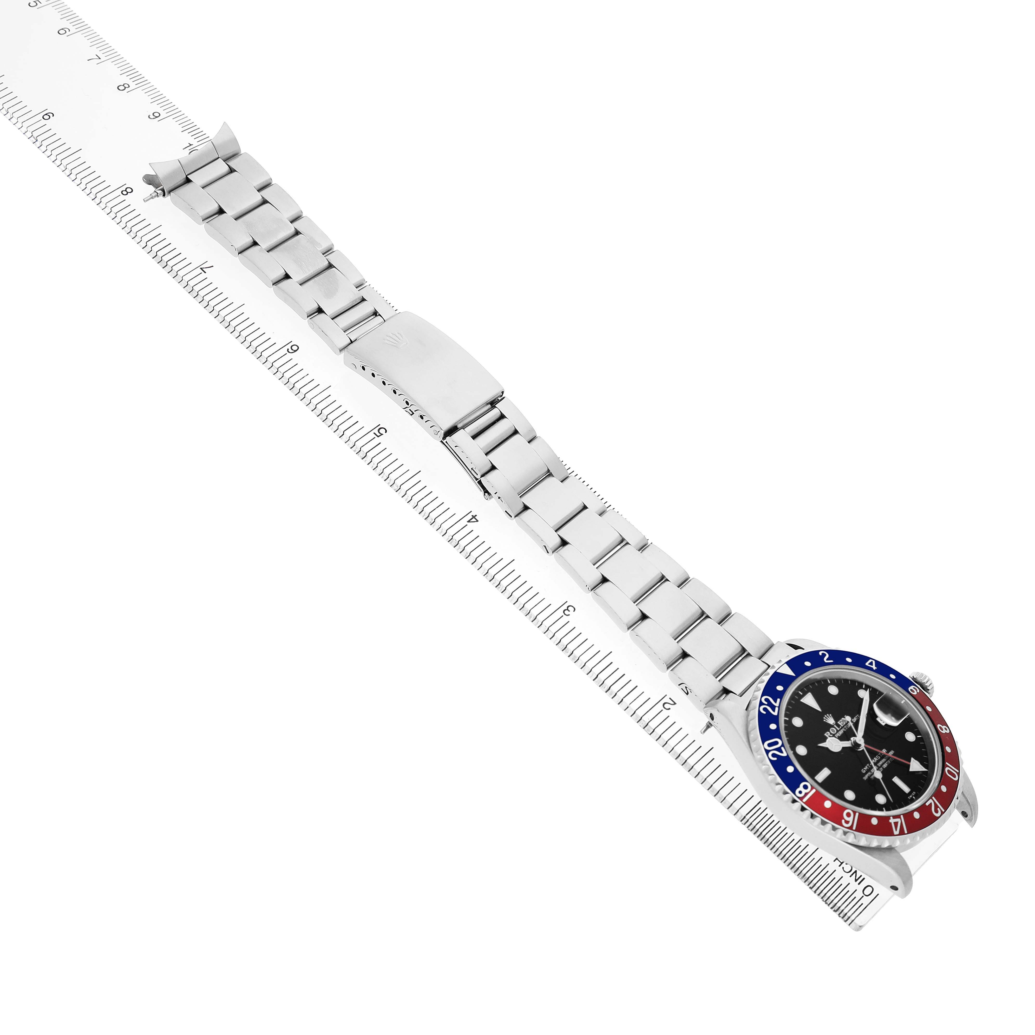 The Rolex GMT-Master 16700 Men's Stainless Steel Black Dial is shown at an angle, featuring the watch face, bezel, and bracelet alongside a ruler for scale.