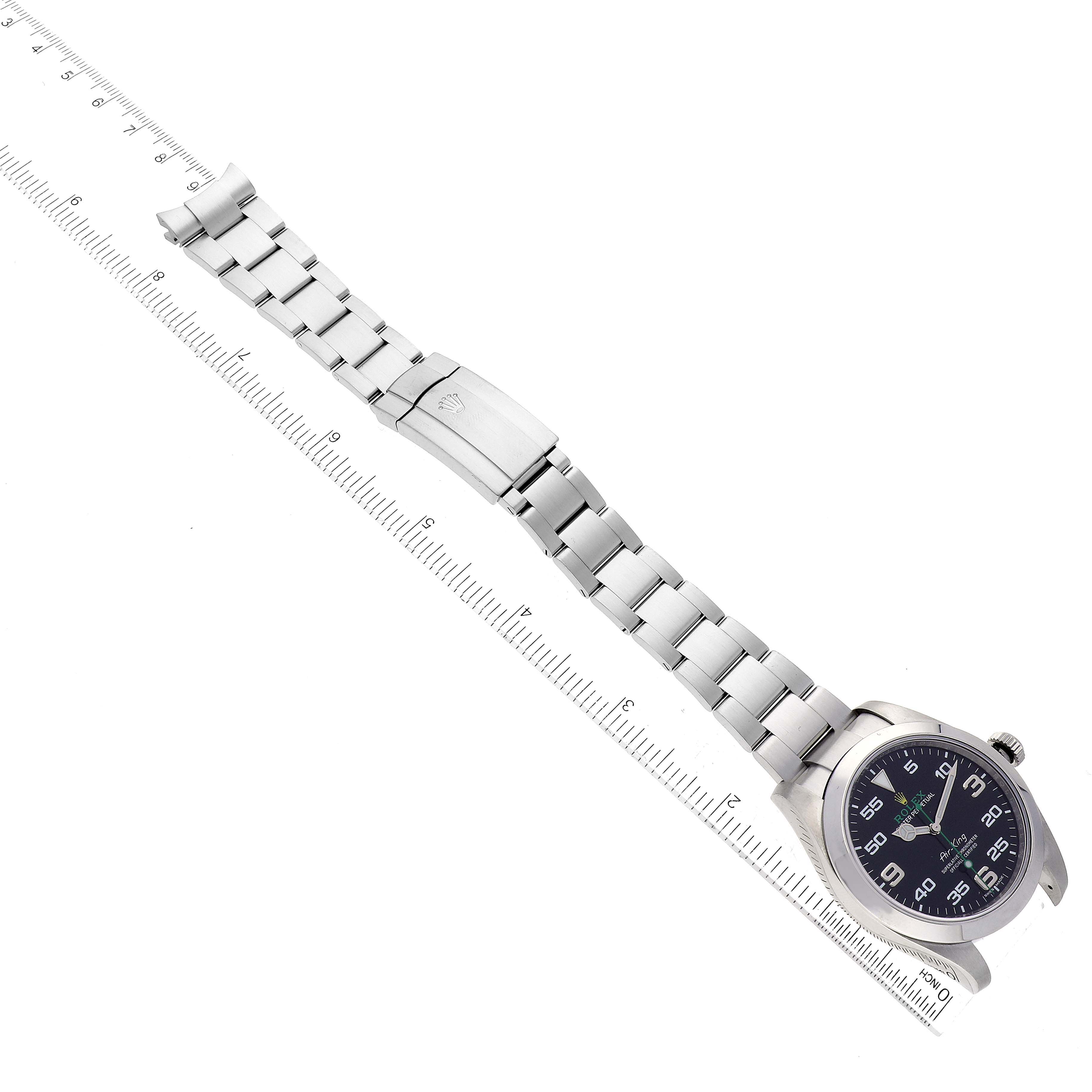 The image shows a top-down view of a Rolex Air-King 116900 Men's Stainless Steel Black Dial 116900 Men's Stainless Steel Black Dial watch, displaying its dial, bezel, band, and clasp next to a ruler.