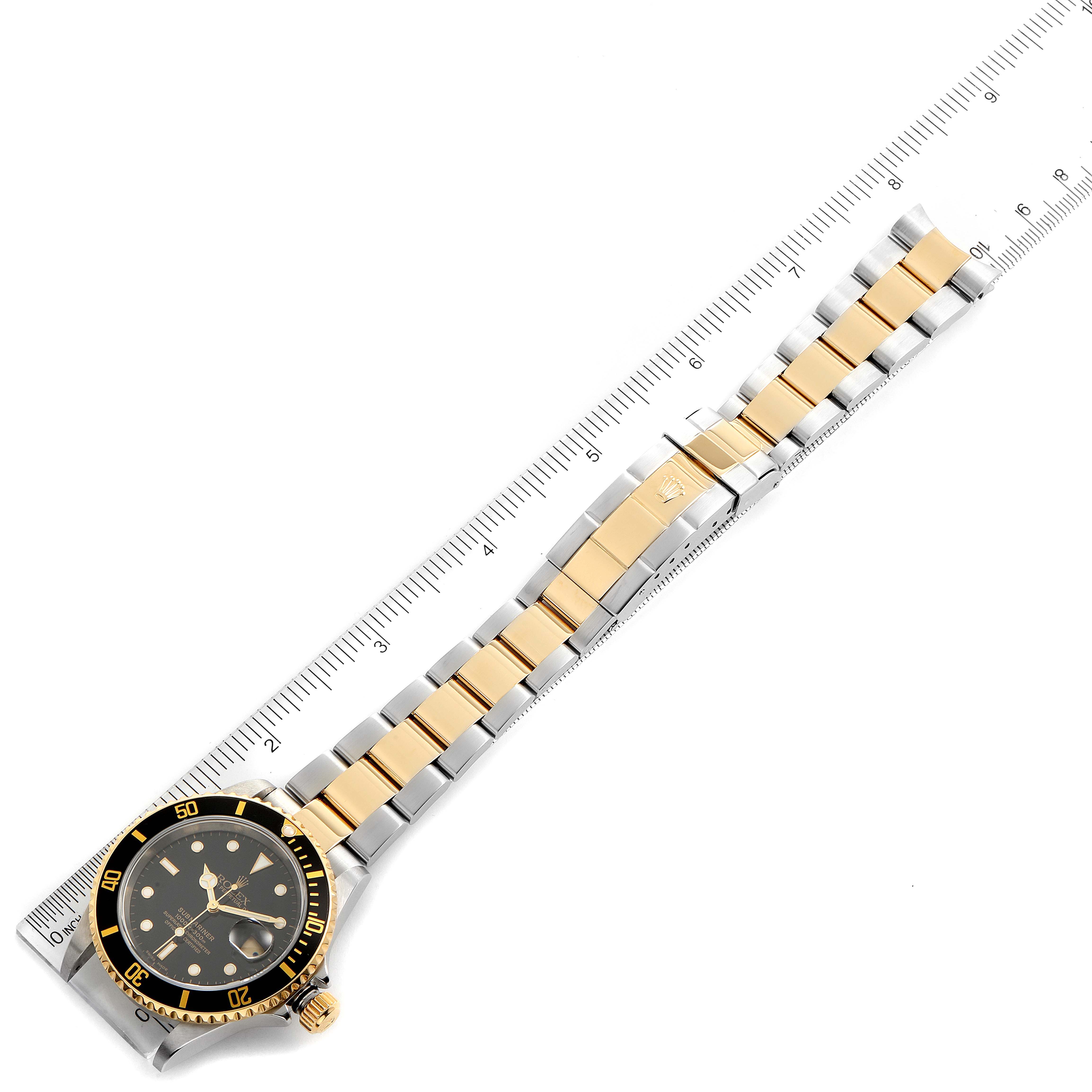 The Rolex Submariner 16613 Men's Steel and Gold (two tone) Black Dial 16613 Men's Steel and Gold (two tone) Black Dial watch is shown from a top-down angle, featuring its dial, bezel, and fully extended bracelet alongside a ruler.
