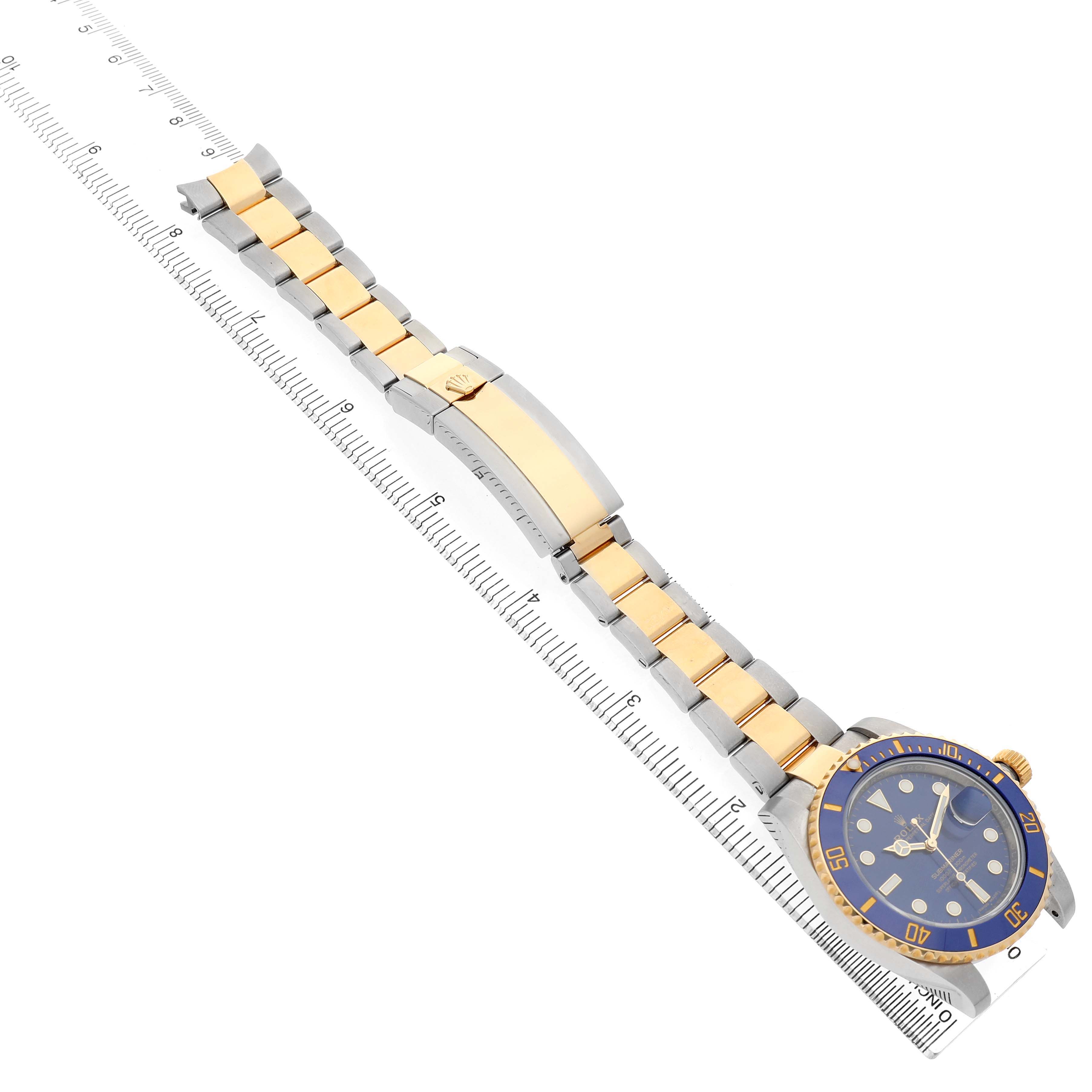 The Rolex Submariner 116613LB Men's Steel and Gold (two tone) Blue Dial is shown at an angled view with its full bracelet and clasp alongside a ruler.