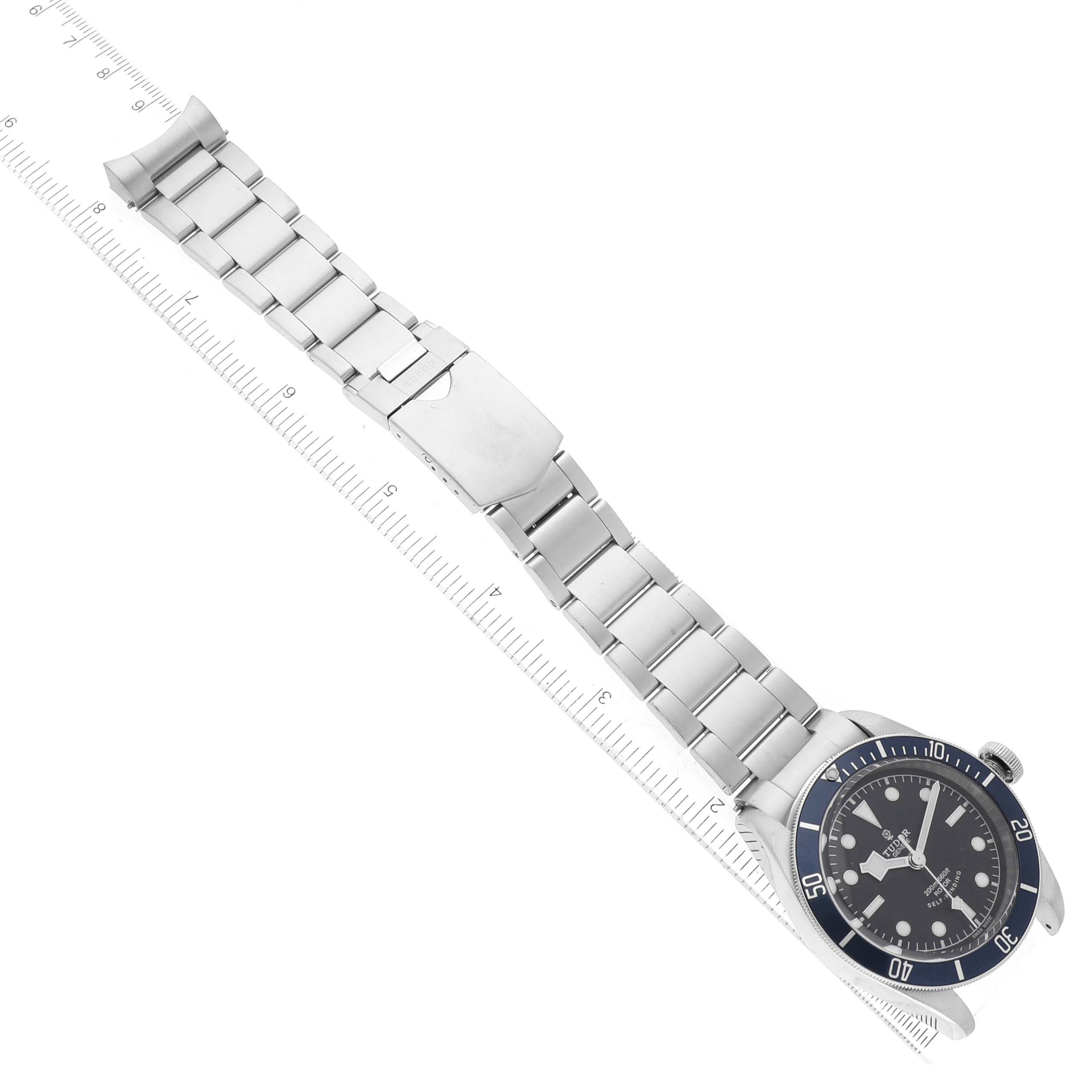 The image shows a Tudor Heritage Black Bay 79220B Men's Stainless Steel Black Dial 79220B Men's Stainless Steel Black Dial watch laid flat with a ruler next to its stainless steel bracelet.