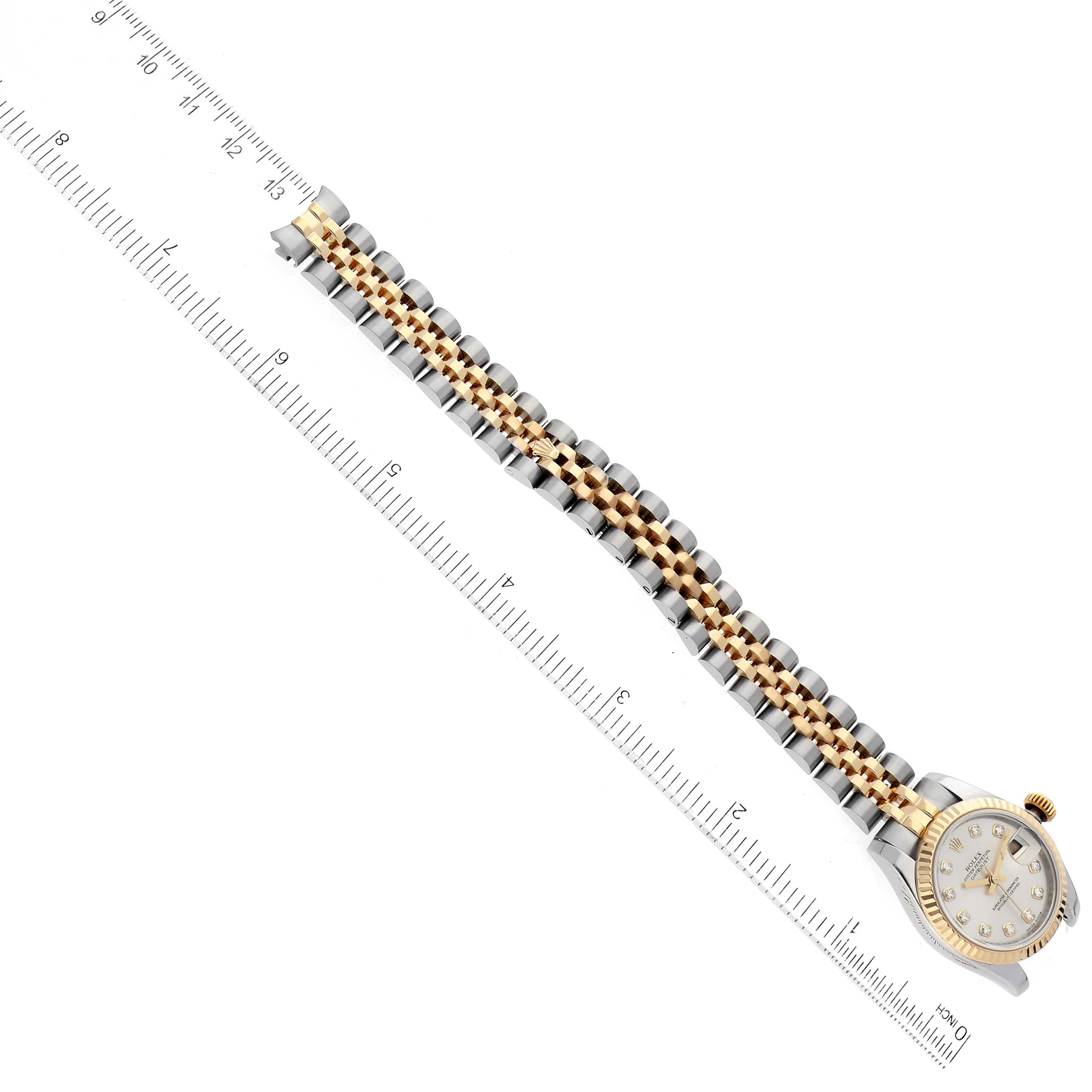 The Rolex Datejust 179173 Men's Steel and Gold (two tone) Silver Dial 179173 Men's Steel and Gold (two tone) Silver Dial watch is shown from an almost top-down angle, displaying the face, crown, and full bracelet alongside a ruler for scale.