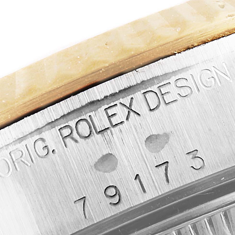 The image shows a close-up of the Rolex Datejust 79173 Women's Steel and Gold (two tone) Blue Dial 79173 Women's Steel and Gold (two tone) Blue Dial model's case, featuring the engraved 'ROLEX DESIGN' text and serial number.