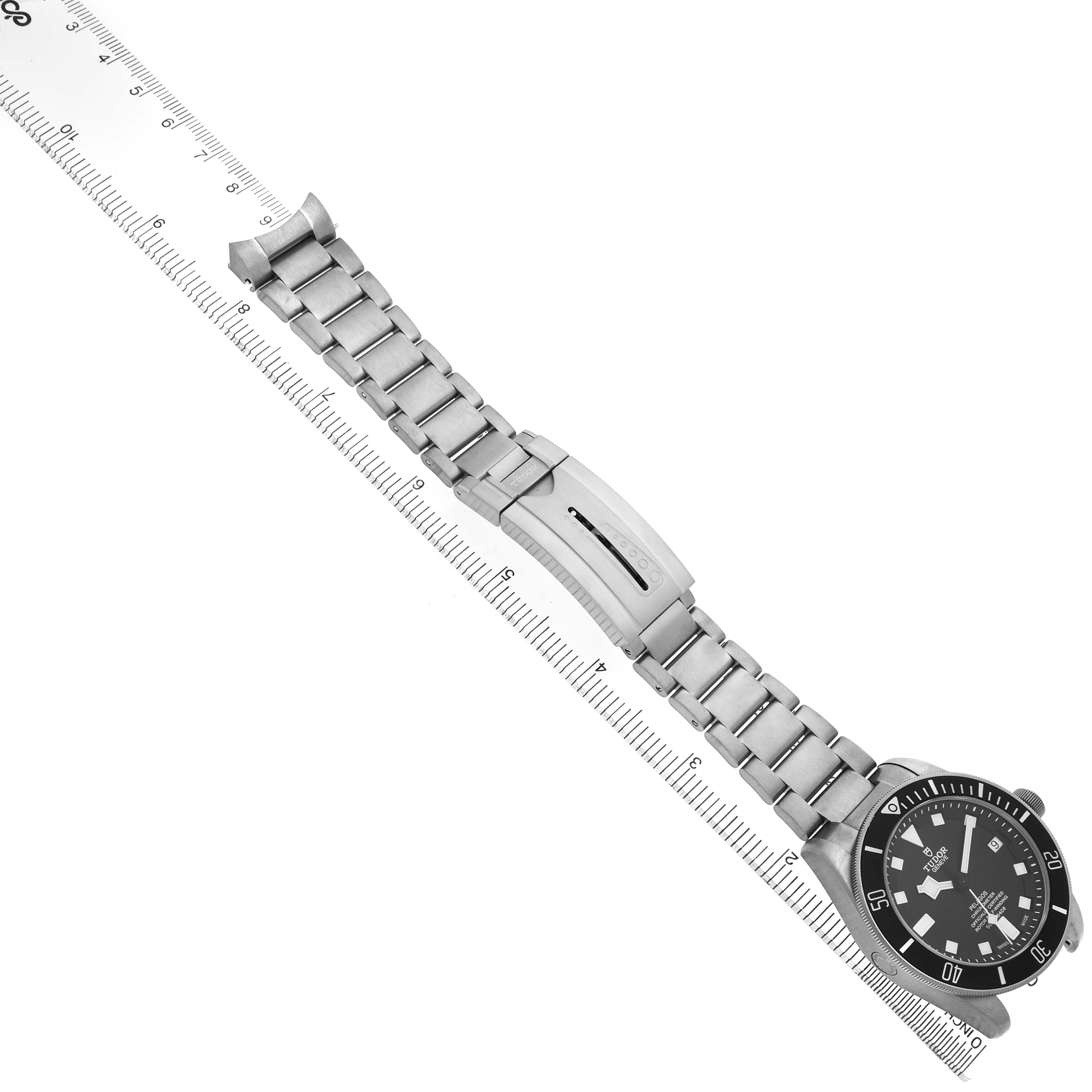 The Tudor Heritage Chrono 25600TN Men's Titanium Black Dial watch is shown from a top-down angle, displaying its bracelet and clasp alongside a ruler for scale.