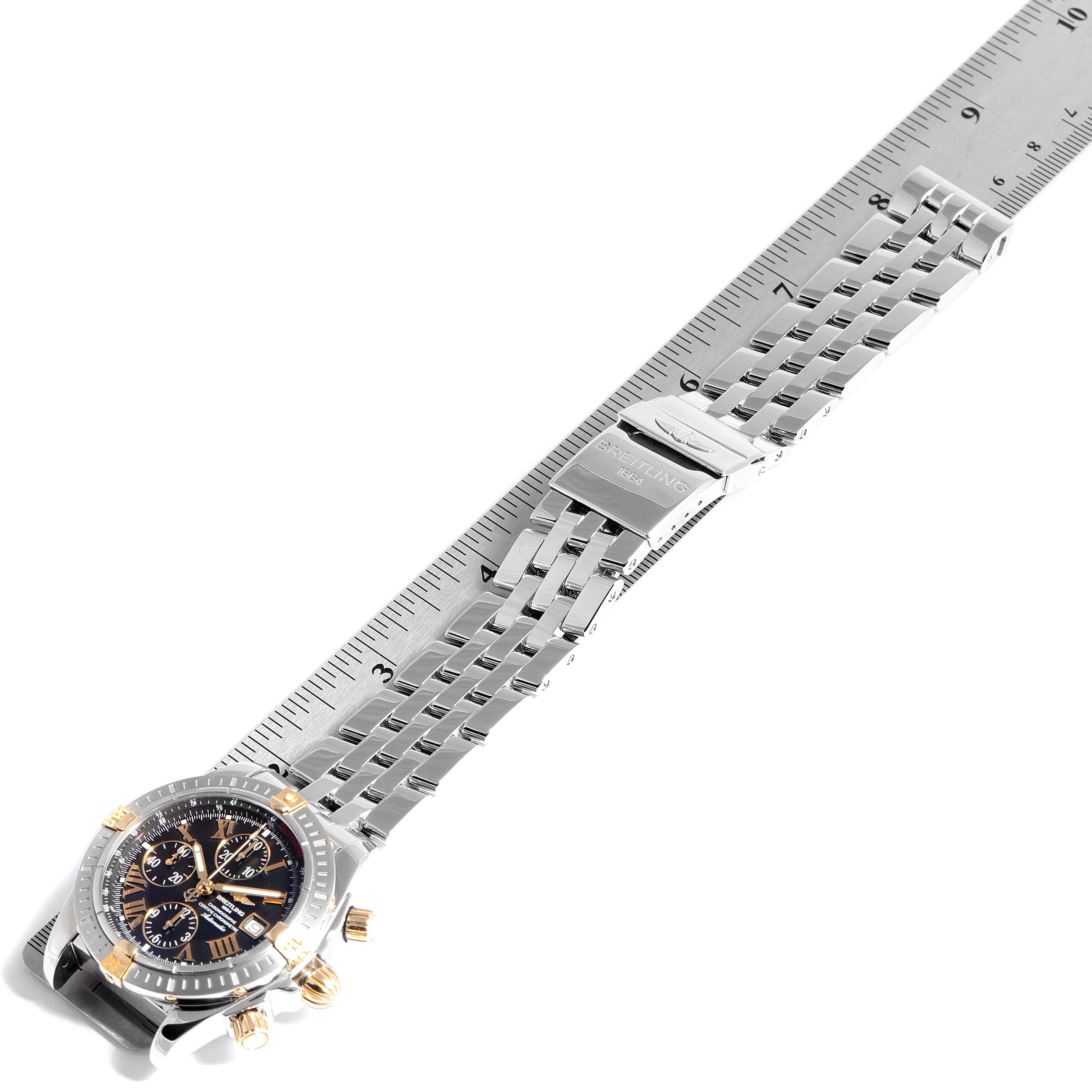 The Breitling Chronomat B13356 Men
s Steel and Gold (two tone) Black Dial B13356 Men
s Steel and Gold (two tone) Black Dial watch is shown from an angled top-down view, exhibiting its face, bezel, and metal bracelet next to a ruler.