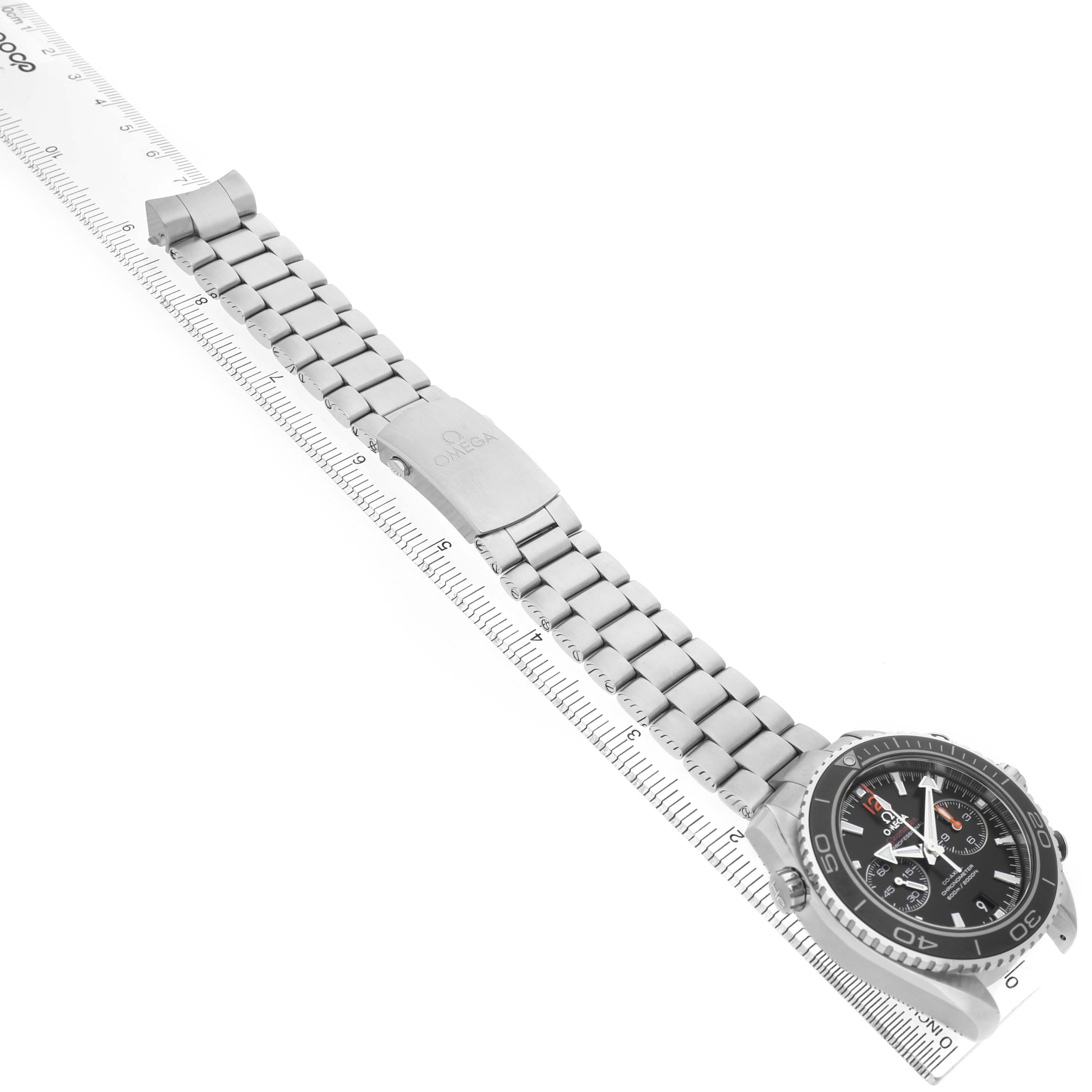 The Omega Planet Ocean 232.30.42.21.01.003 Men's Stainless Steel Black Dial watch is shown from an angled top view, highlighting its face and metal bracelet alongside a ruler.