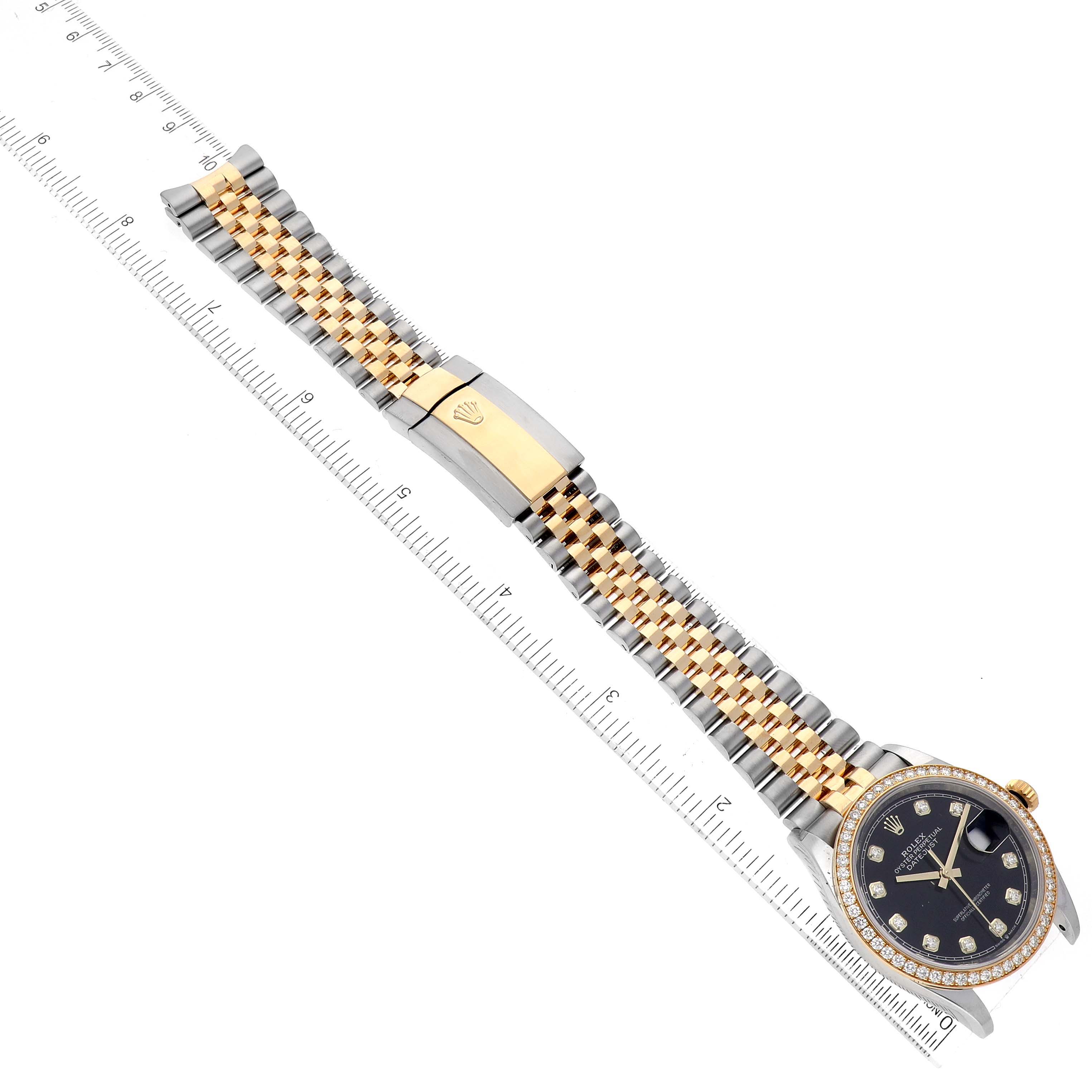 The image shows a Rolex Datejust M126283RBR-0003 Men's Steel and Gold (two tone) Black Dial M126283RBR-0003 Men's Steel and Gold (two tone) Black Dial watch with a Jubilee bracelet and clasp fully extended alongside a ruler.