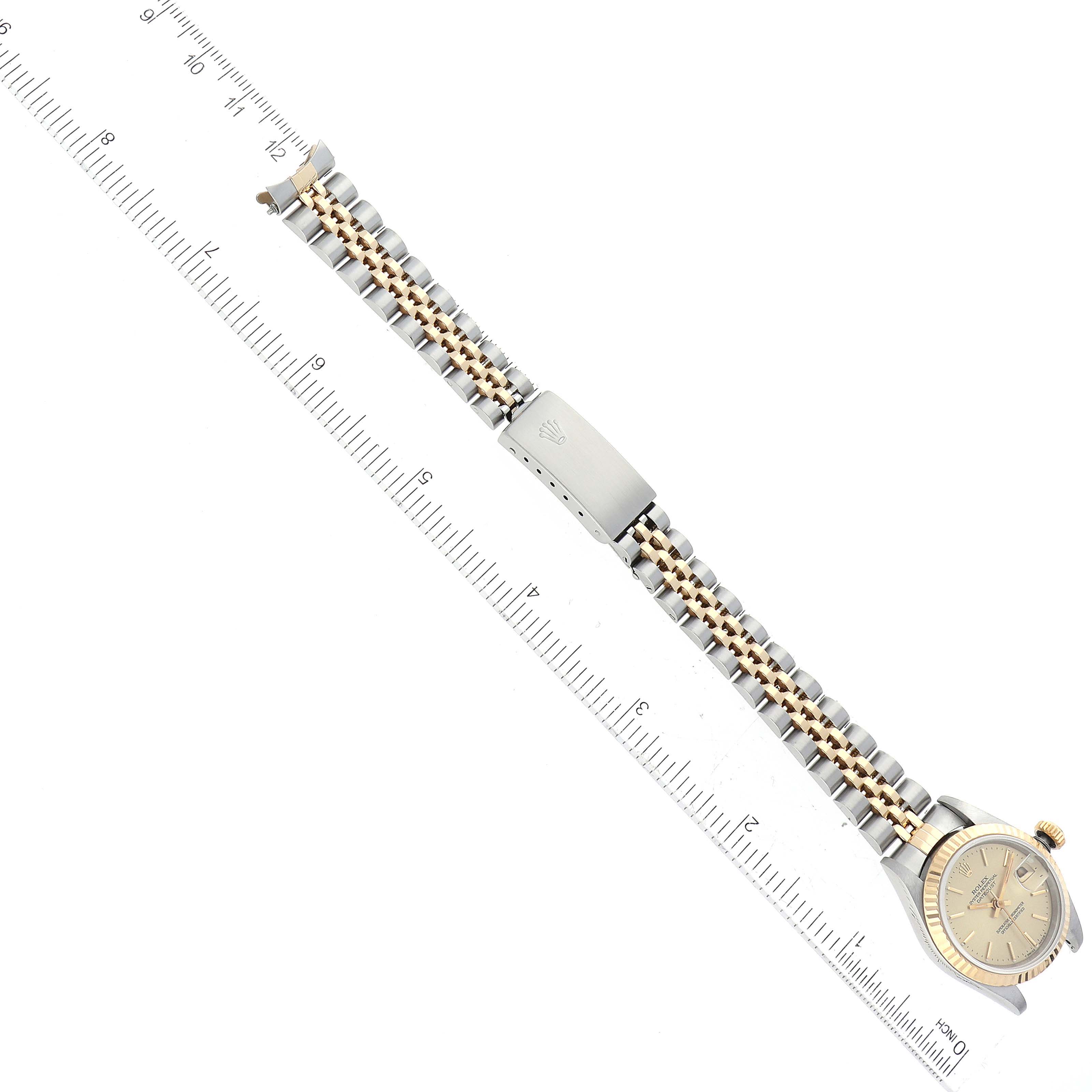 The image shows a Rolex Datejust 69173 Women's Steel and Gold (two tone) Champagne Dial 69173 Women's Steel and Gold (two tone) Champagne Dial watch laying flat with its band stretched out and a ruler aligned parallel to it.