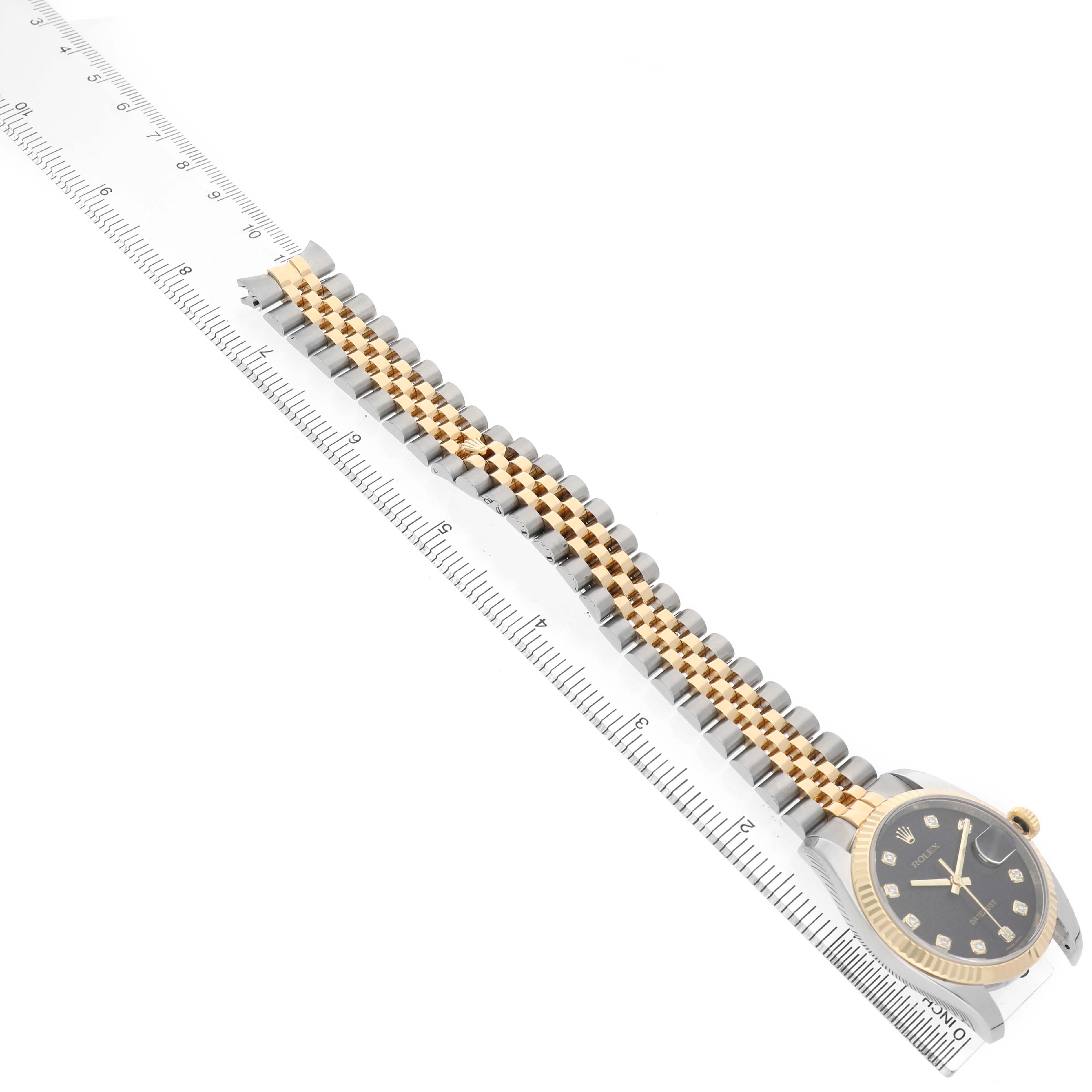 The Rolex Datejust 116233 Men's Steel and Gold (two tone) Black Dial watch is shown at a diagonal angle, highlighting the bracelet and face, with a ruler beside it for scale.