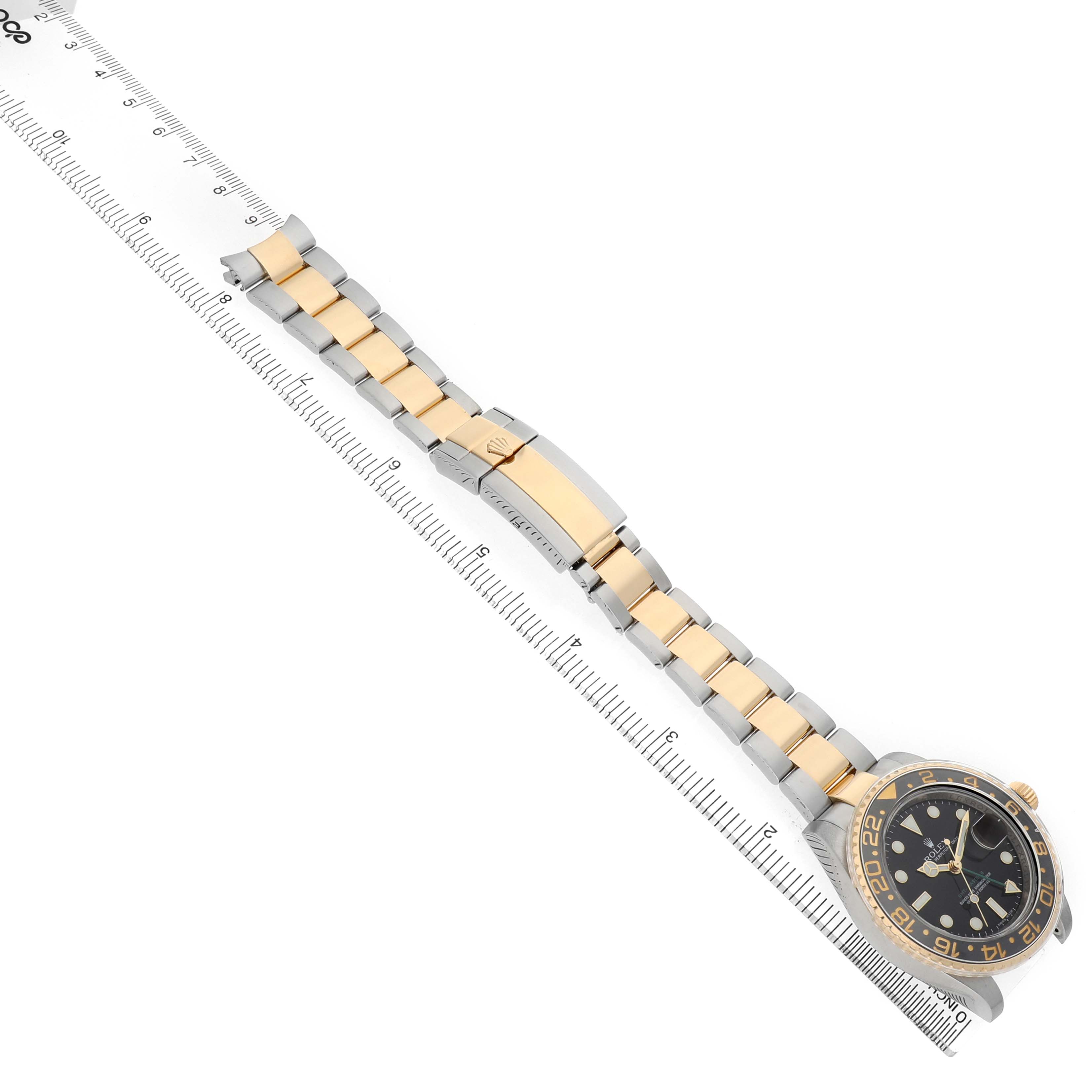The Rolex GMT-Master M116713LN Men's Steel and Gold (two tone) Black Dial watch is shown from a top-down angle, displaying the full bracelet and clasp alongside a measuring ruler.