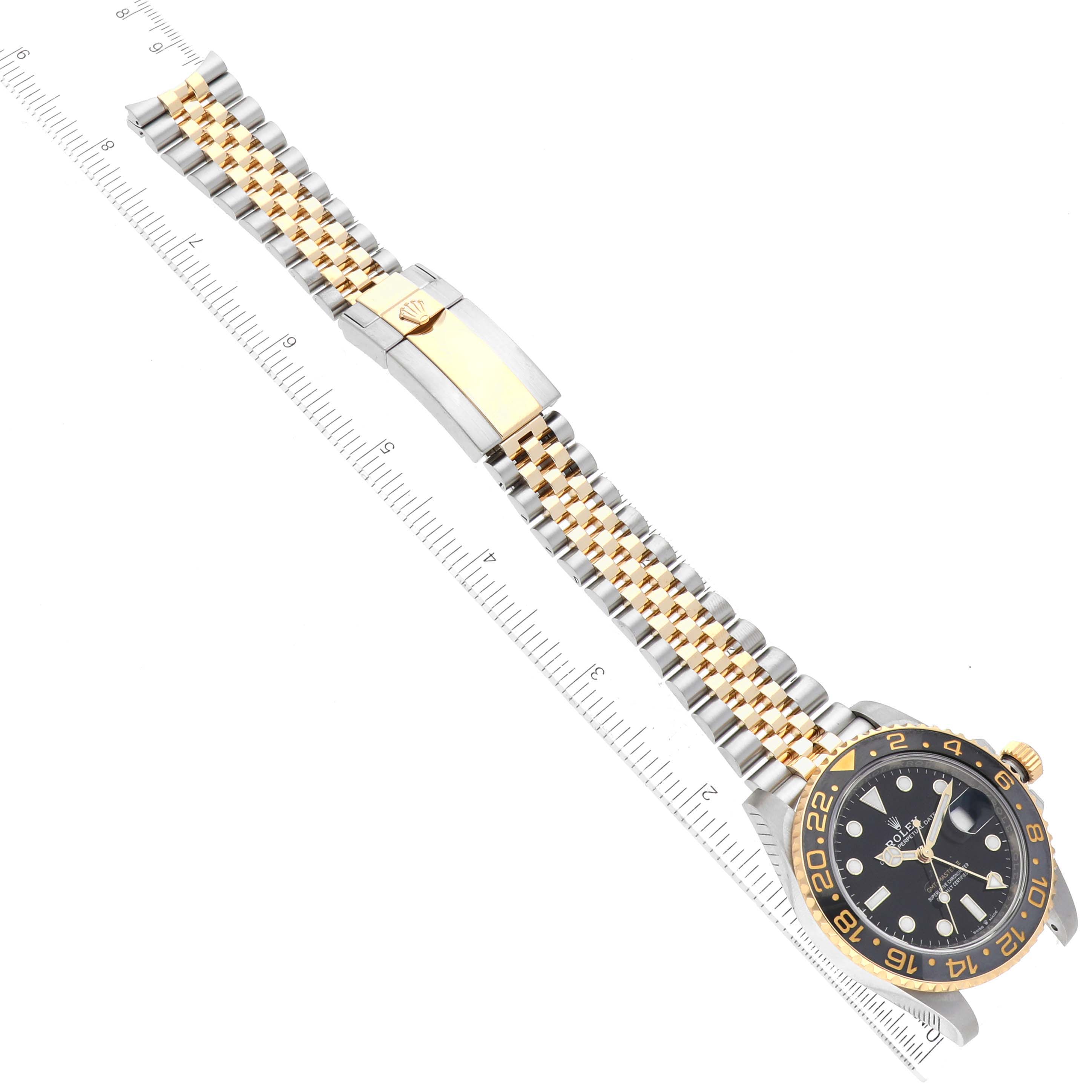 This image shows a top-down view of the Rolex GMT-Master 126713 Men's Steel and Gold (two tone) Black Dial 126713 Men's Steel and Gold (two tone) Black Dial watch, featuring the dial, bezel, and bracelet clasp laying flat next to a ruler.