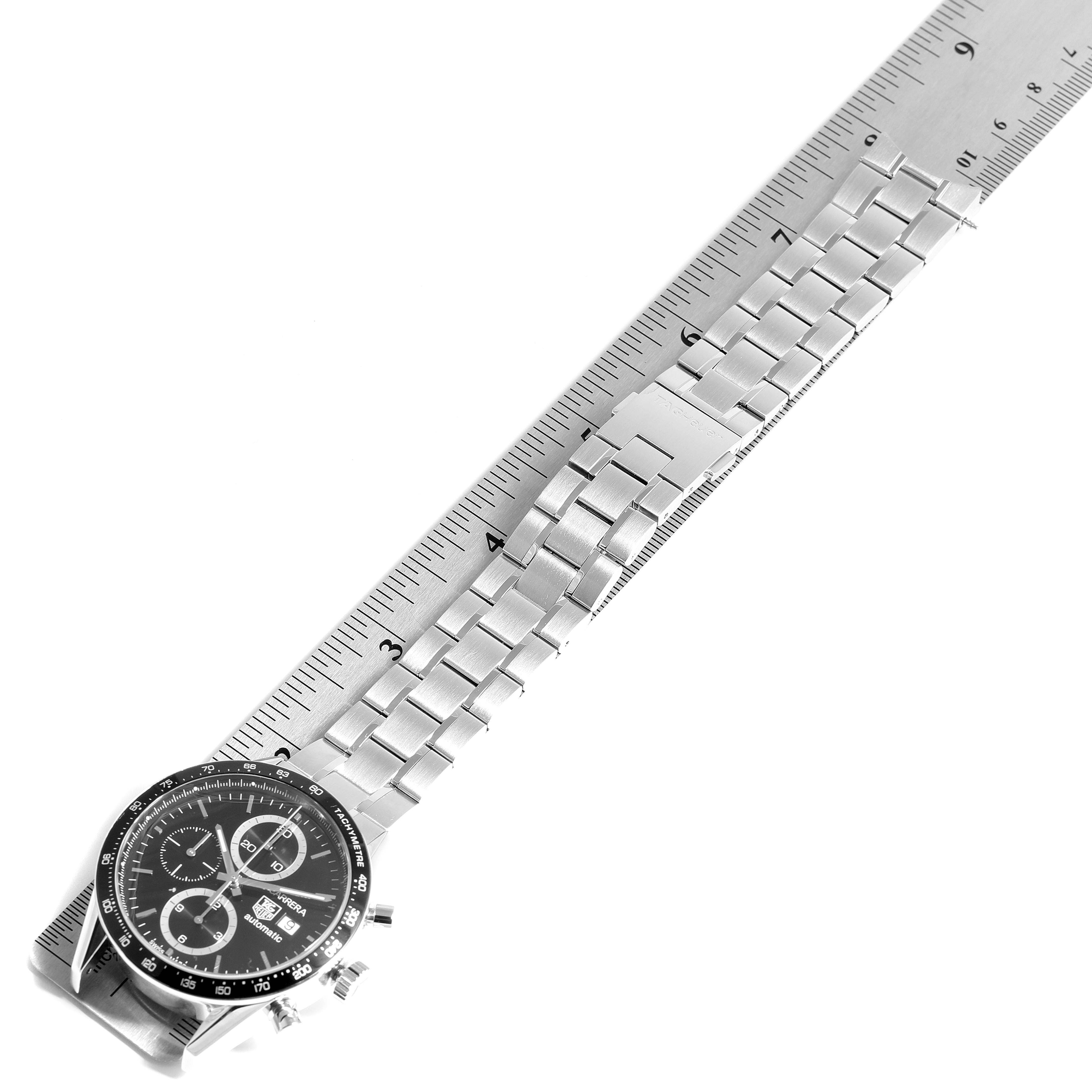 The image shows a Tag Heuer Carrera CV2010-3 Men
s Stainless Steel Black Dial CV2010-3 Men
s Stainless Steel Black Dial watch from a top-down angle, highlighting its face and metal bracelet alongside a measuring scale.