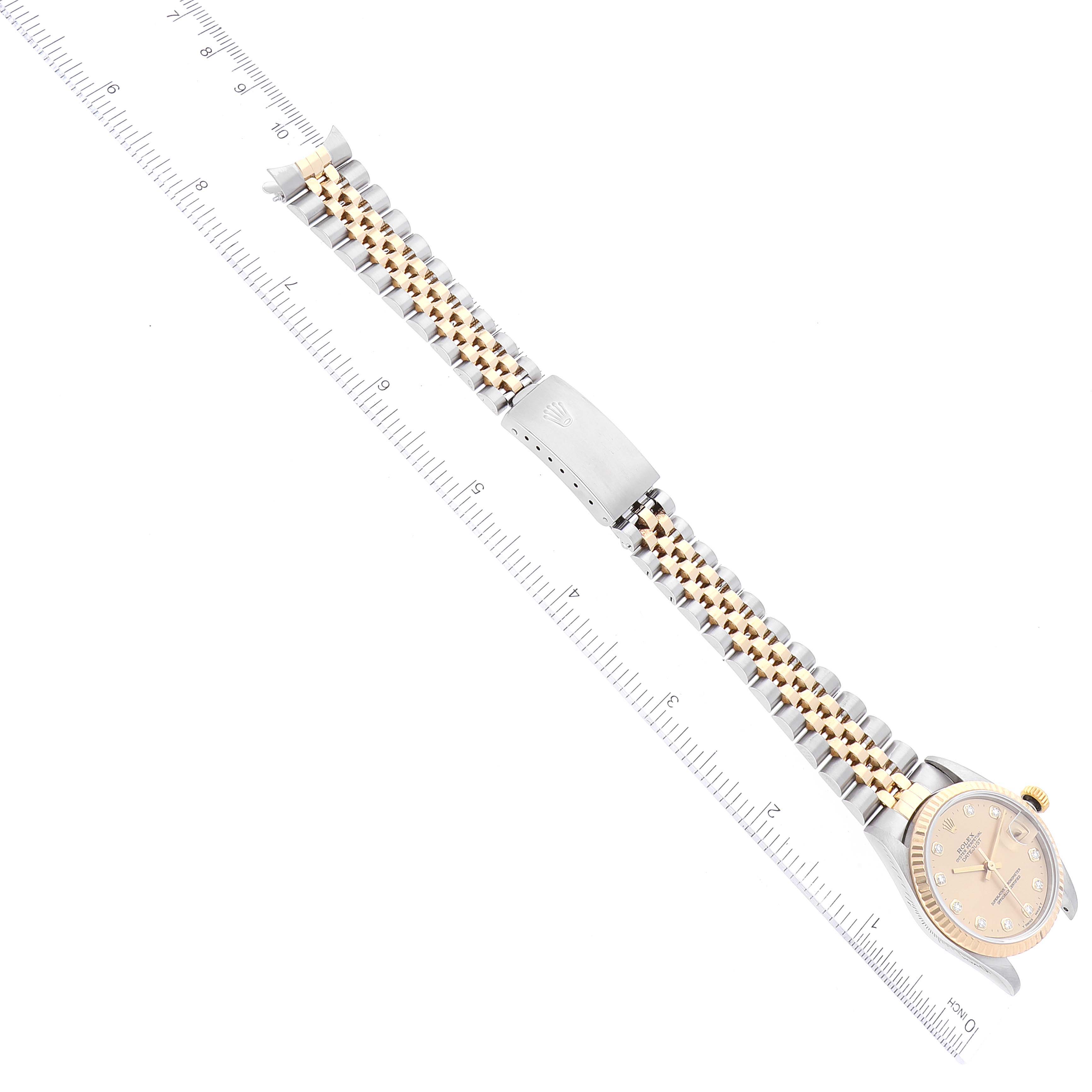 The image shows a top view of a Mid-Size Rolex watch
s dial, bracelet, and clasp alongside a ruler for scale.
