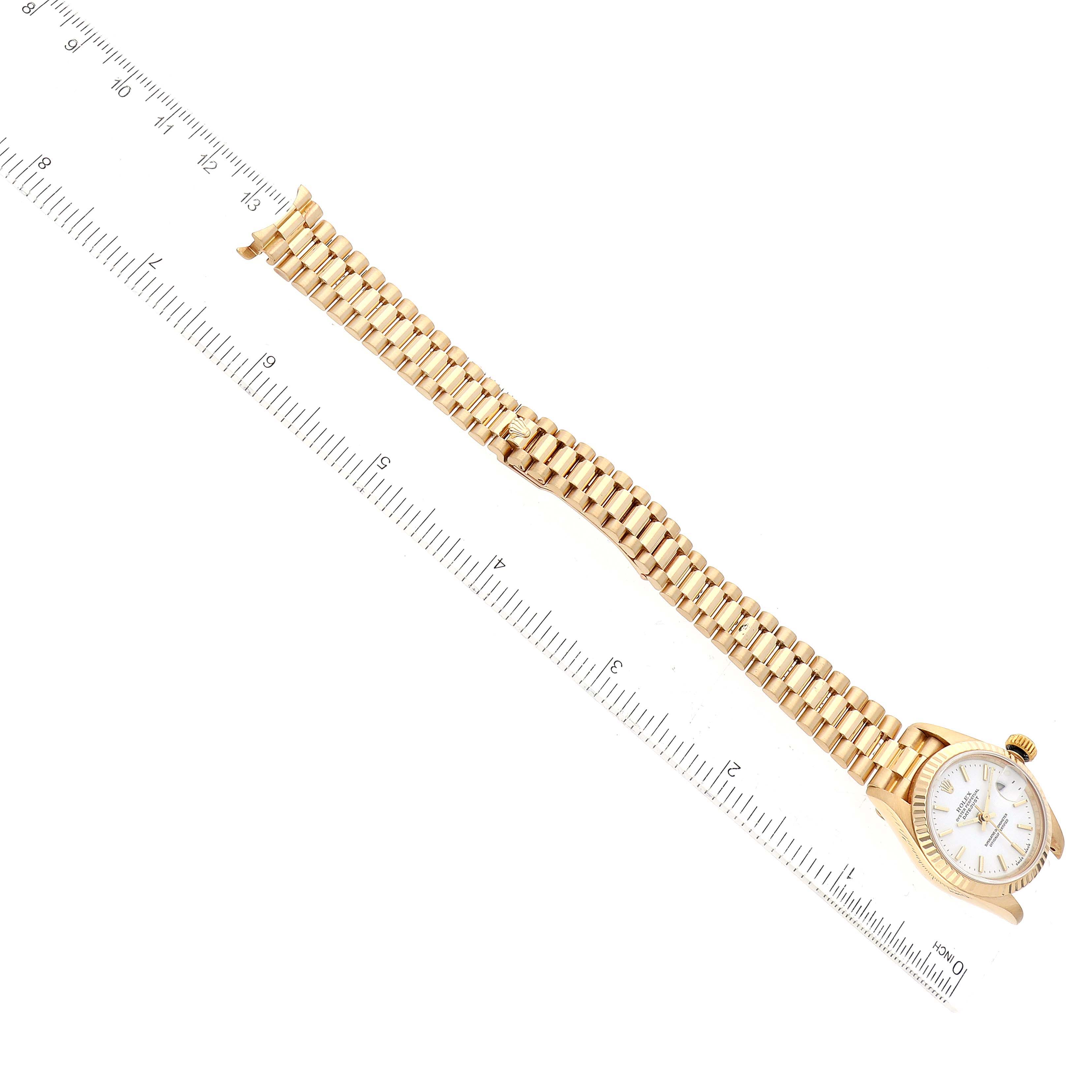 The Rolex President 69178 Women's Yellow Gold White Dial 69178 Women's Yellow Gold White Dial watch is shown from an overhead perspective, highlighting the face and gold bracelet, with a ruler beside it.