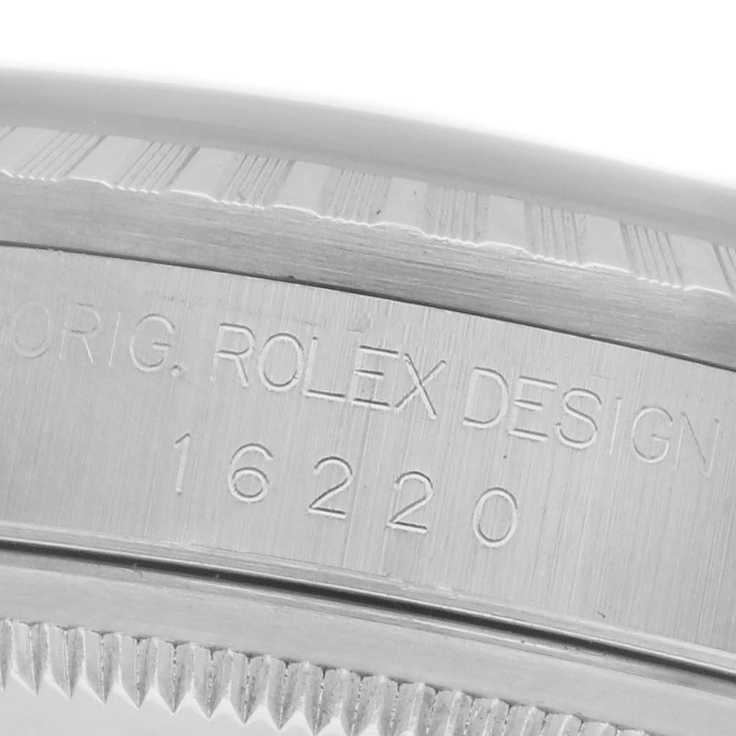 The image shows a close-up of a Rolex Datejust 16220 Men
s Stainless Steel Silver Dial 16220 Men
s Stainless Steel Silver Dial watch case side with engravings of "ORIG. ROLEX DESIGN" and the model number "16220".