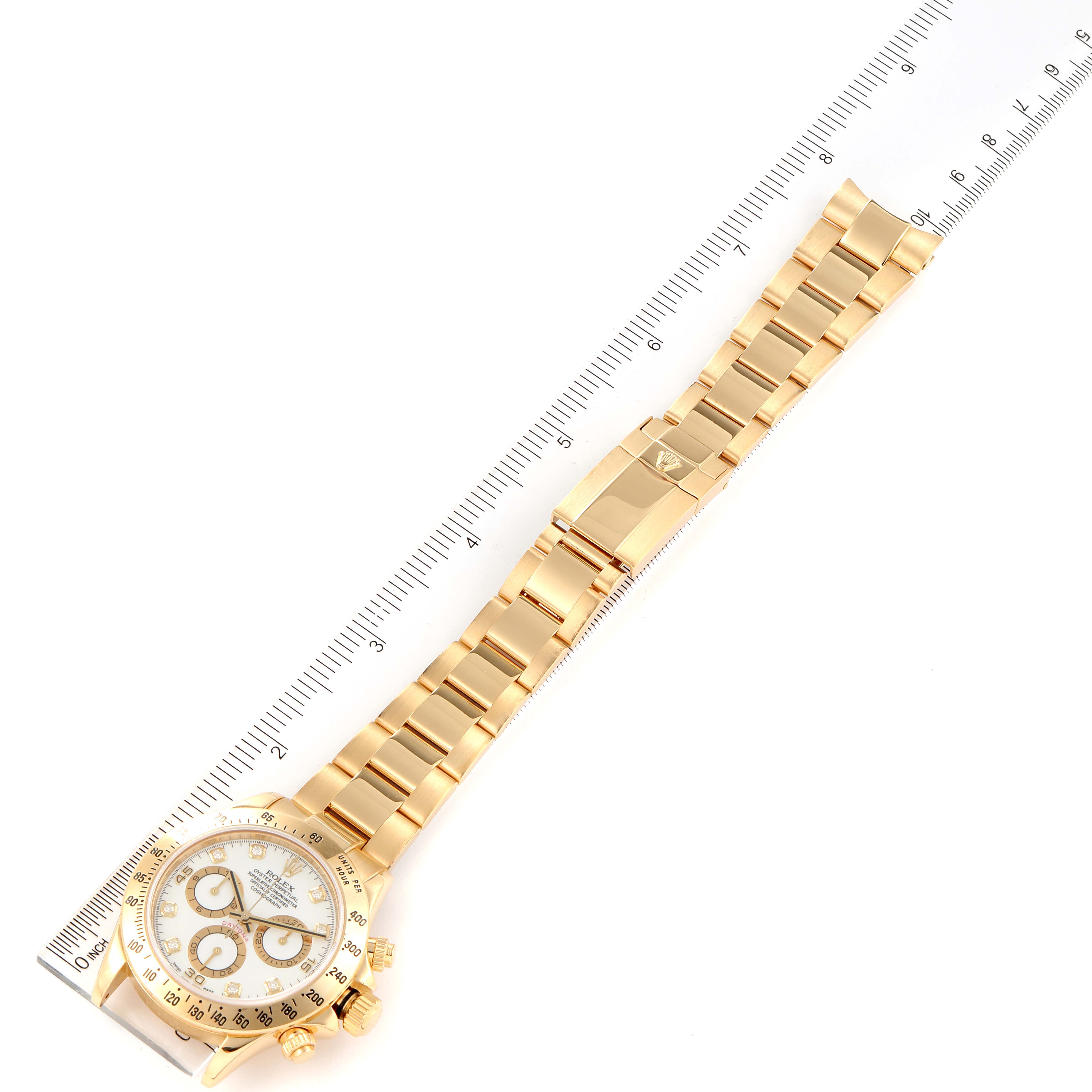 The image shows a gold Rolex Daytona 116528 Men's Yellow Gold White Dial 116528 Men's Yellow Gold White Dial watch laid flat, with its face, band, and clasp visible next to a ruler.