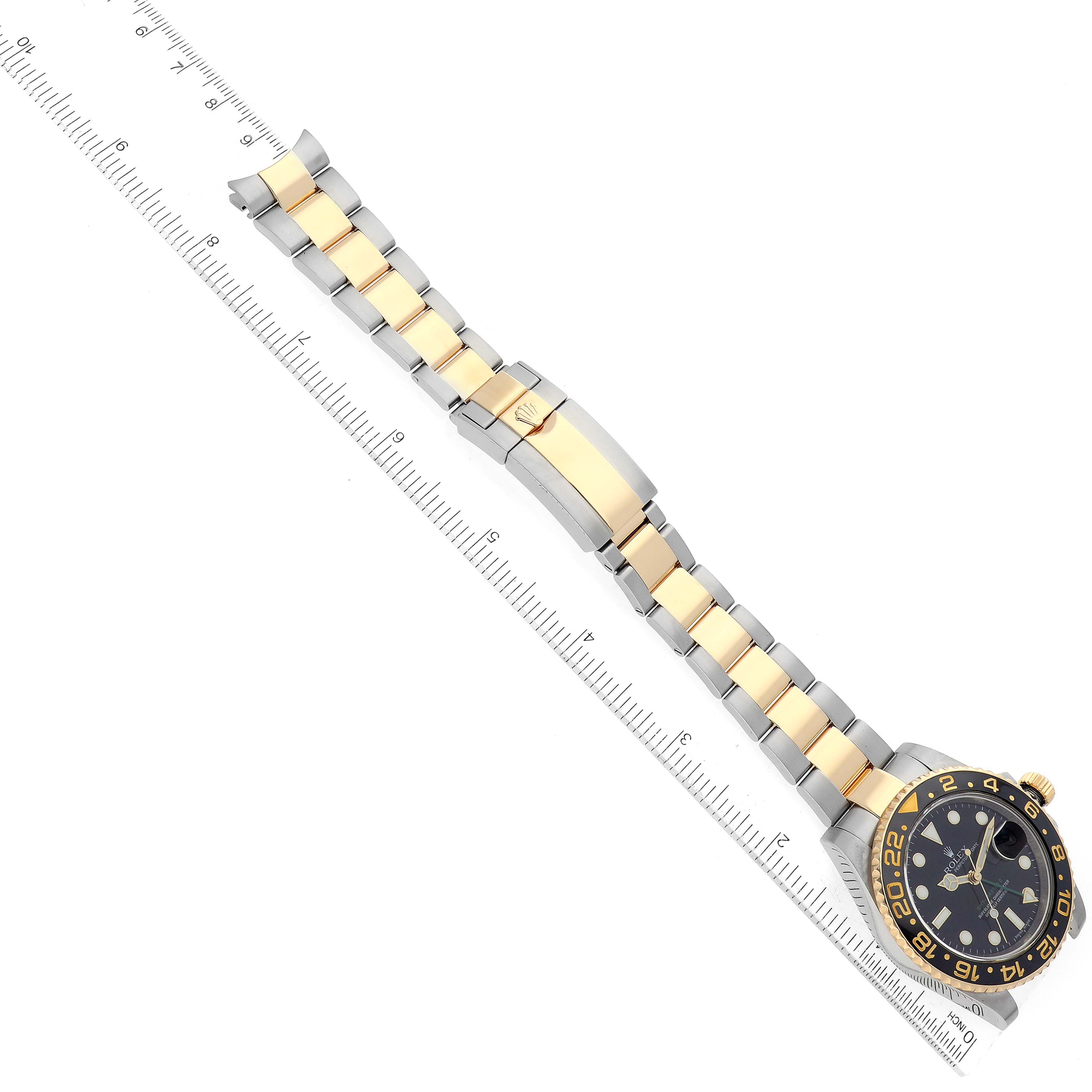 This image shows an overhead view of a Rolex GMT-Master 116713 Men's Steel and Gold (two tone) Black Dial 116713 Men's Steel and Gold (two tone) Black Dial watch including its face and metal bracelet with a ruler for scale.