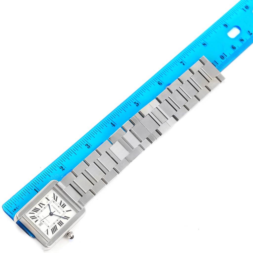 The image shows a Cartier Tank Solo W5200028 Men
s Stainless Steel Silver Dial W5200028 Men
s Stainless Steel Silver Dial watch placed beside a blue ruler, displaying its rectangular face and metal bracelet.