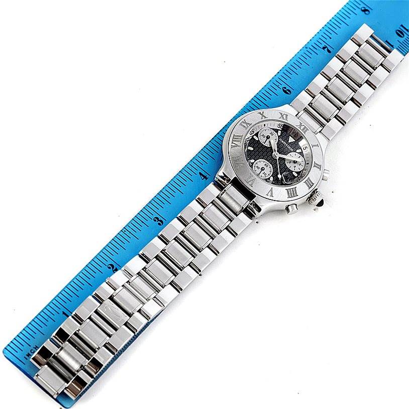 The image shows a top-down view of a Cartier Must 21 Chronoscaph W10172T2 Men's Stainless Steel Black Dial W10172T2 Men's Stainless Steel Black Dial watch alongside a blue ruler, highlighting its face and metal band.