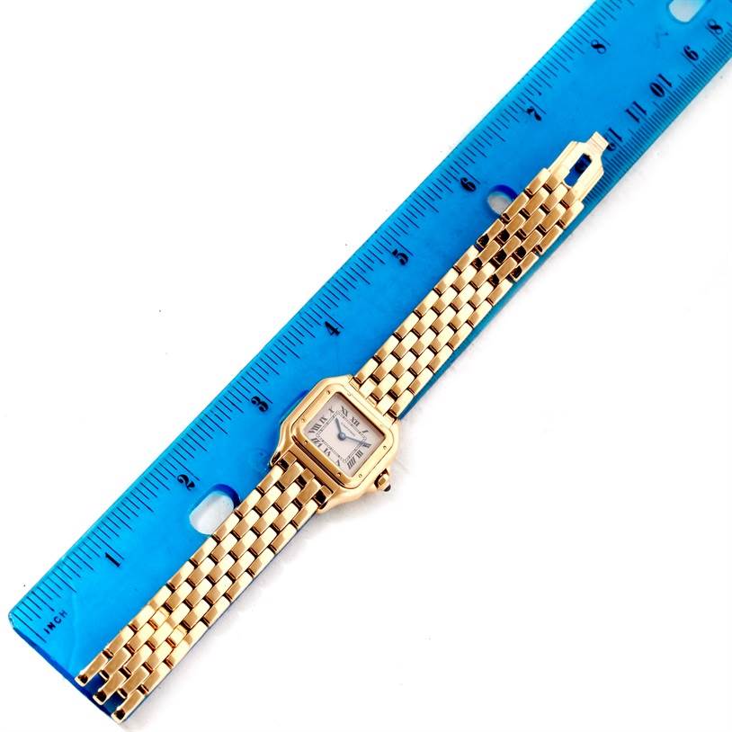 The image shows a Panthere model by Cartier, laid flat next to a blue ruler, displaying its face and gold bracelet.