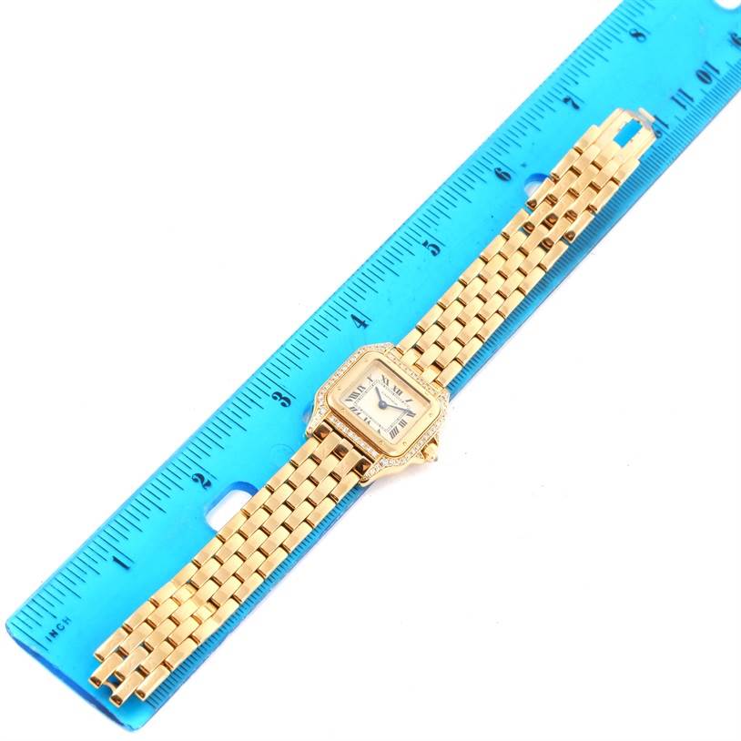 The Cartier Panthere W25022B9 Women's Yellow Gold Silver Dial W25022B9 Women's Yellow Gold Silver Dial watch is displayed face-up with its gold band laid out straight alongside a blue ruler.