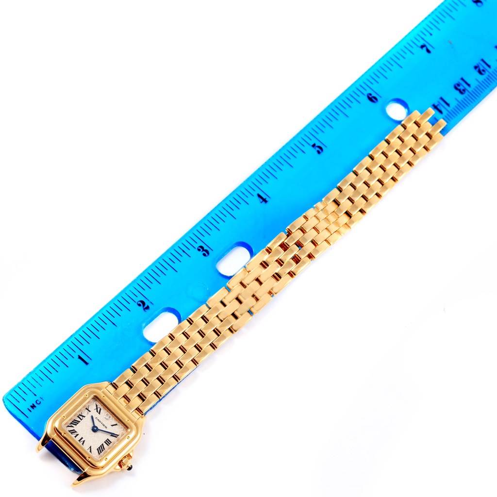 The image shows a Panthere model Cartier watch from a top-down angle, featuring its gold bracelet and part of its face with a measuring ruler beside it.