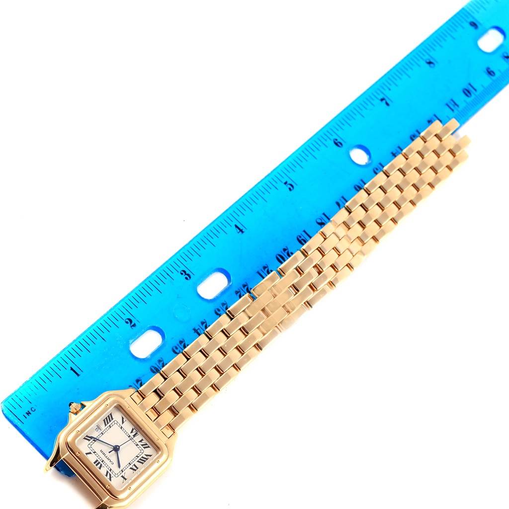 The Cartier Panthere W25014B9 Men's Yellow Gold Silver Dial W25014B9 Men's Yellow Gold Silver Dial watch is shown from a top-down angle, highlighting its face, case, and a portion of its bracelet next to a blue ruler.