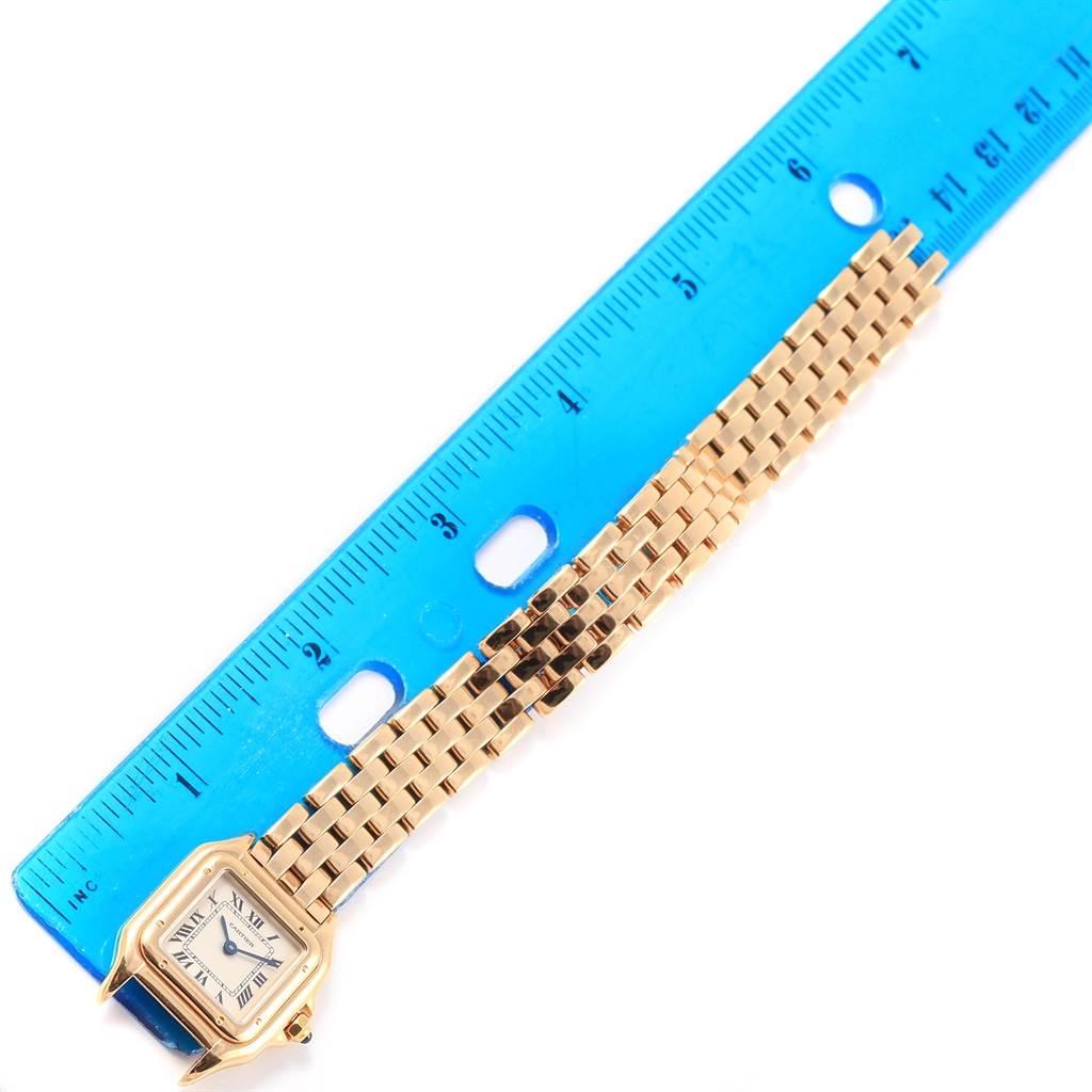 The Cartier Panthère model watch is shown from above, with its gold face, bezel, and linked bracelet, next to a ruler.