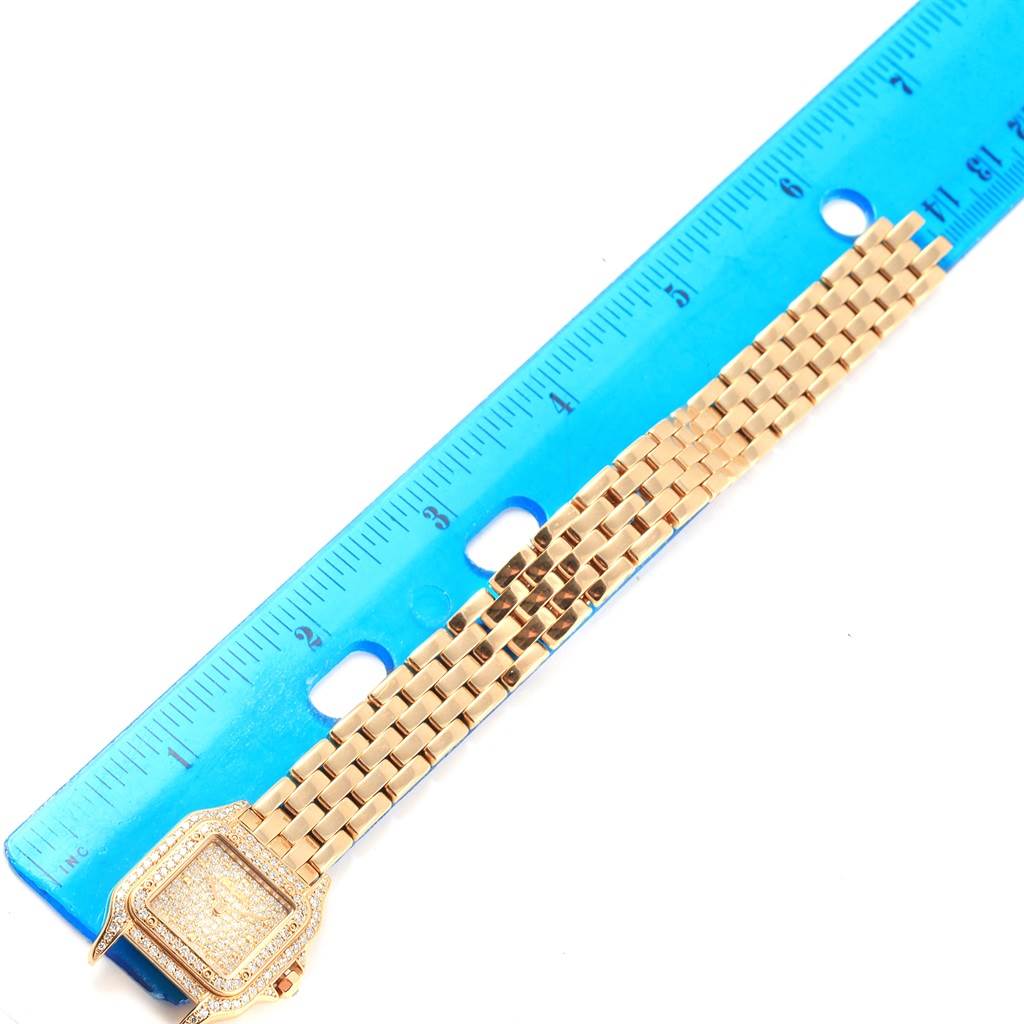 The image shows a Cartier Panthere Women's Yellow Gold Champagne Dial Women's Yellow Gold Champagne Dial watch placed next to a blue ruler, displaying its face and part of its gold bracelet.