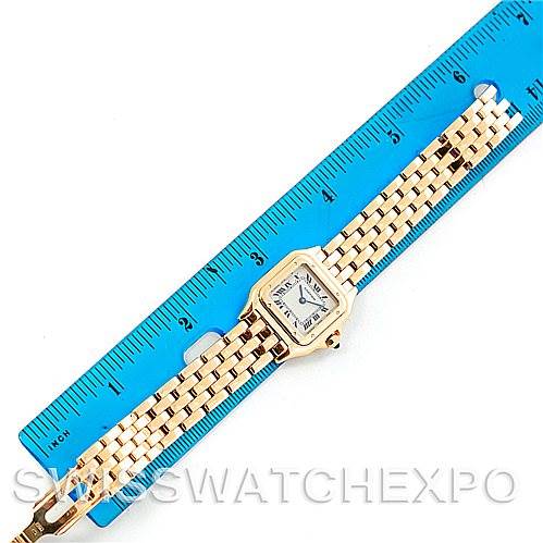 The Cartier Panthere W25022B9 Women
s Yellow Gold Silver Dial W25022B9 Women
s Yellow Gold Silver Dial watch is shown from a top-down angle, lying next to a blue ruler, displaying its face and gold bracelet.