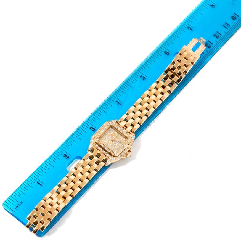 The image shows a Panthere de Cartier watch placed on a blue ruler, displaying its gold bracelet and diamond-encrusted face from above.