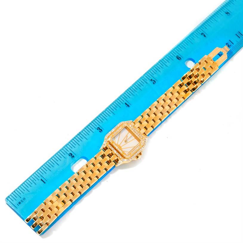 The image shows a gold Panthere model watch by Cartier laid flat against a blue ruler, measured for length.