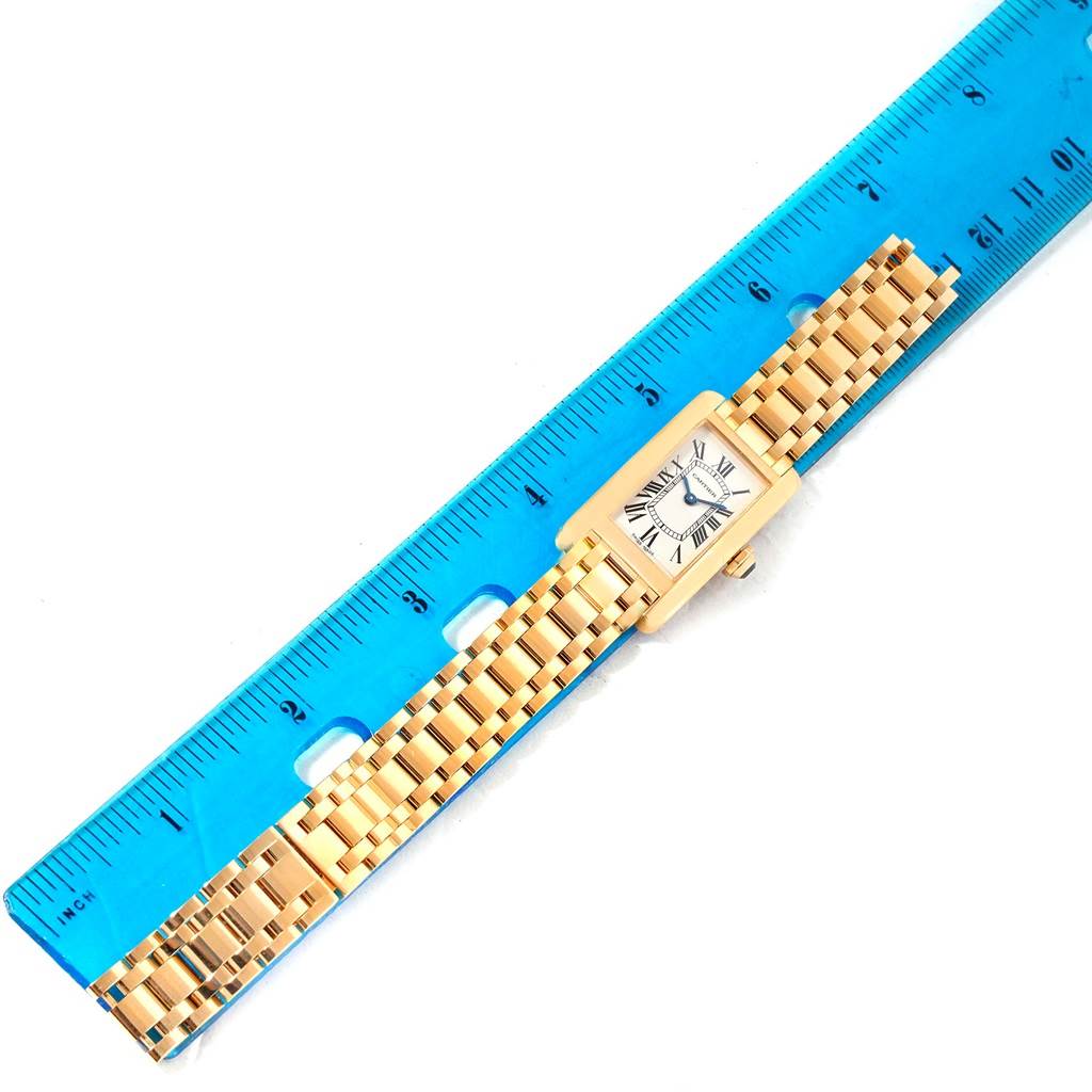 The Tank Americaine by Cartier is shown flat with a blue ruler below, featuring its face, bezel, and bracelet.