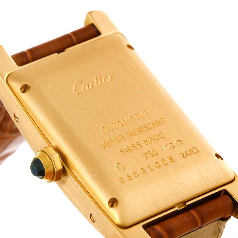 This image shows the back of the Cartier Tank Americaine W2603556 Women's Yellow Gold Silver Dial W2603556 Women's Yellow Gold Silver Dial watch, highlighting the inscriptions and part of the strap.