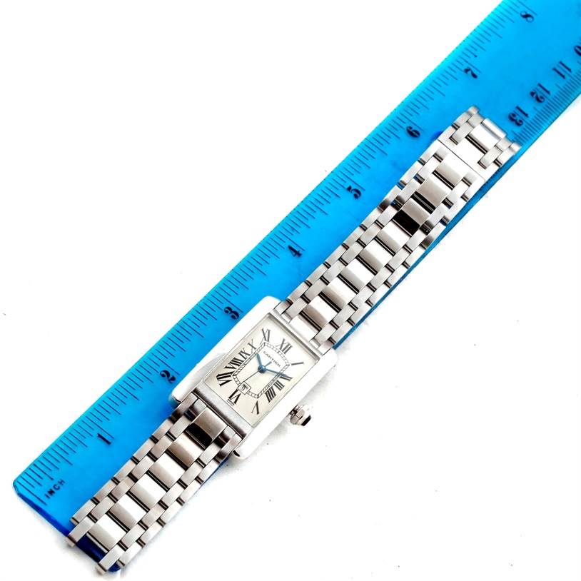 The Cartier Tank Americaine W26036L1 Women's White Gold Silver Dial W26036L1 Women's White Gold Silver Dial watch is shown from a top-down angle, featuring its face, bracelet, and a blue ruler for scale.