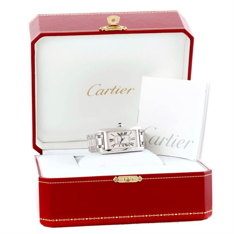 A Cartier Tank Américaine watch is displayed in an open red Cartier box, with instruction manuals beside it.