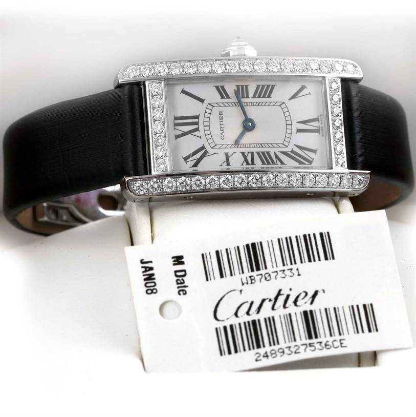 The image shows a Cartier Tank Americaine WB707331 Women
s White Gold Silver Dial WB707331 Women
s White Gold Silver Dial watch face-on, with a black leather strap and diamond-encrusted bezel, alongside a product tag.
