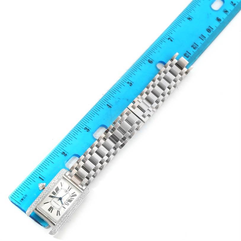 The Tank Américaine watch by Cartier is displayed flat with the face and bracelet visible, alongside a blue ruler for scale.