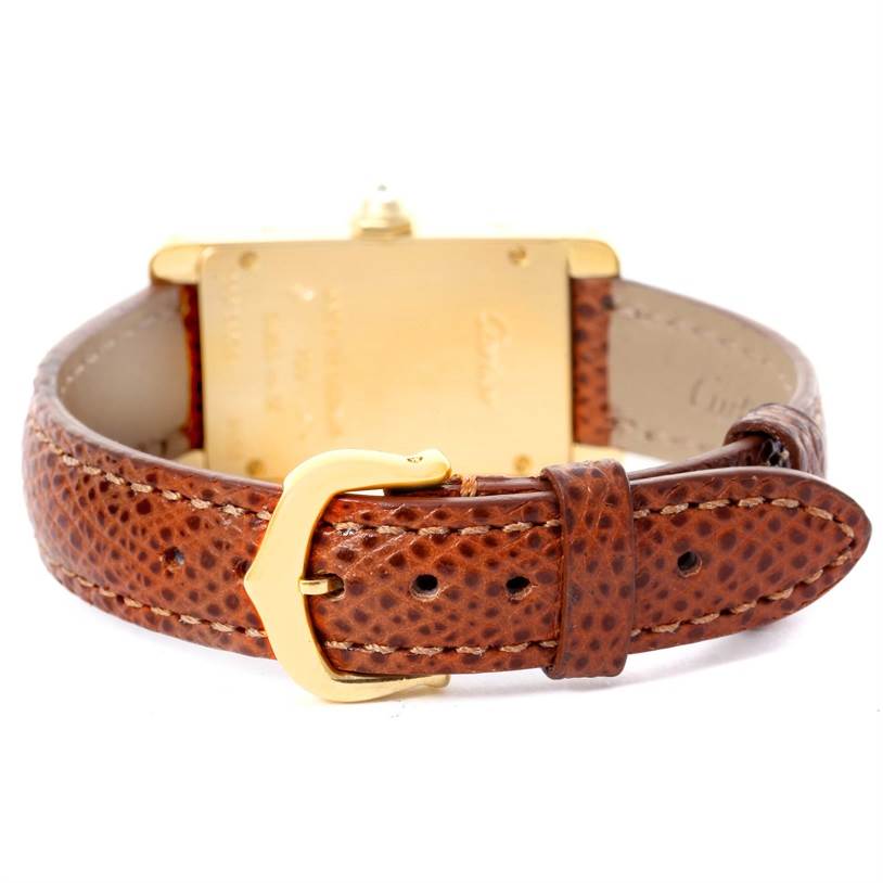 The image shows the back view of a Cartier Tank Americaine WB707231 Women
s Yellow Gold Silver Dial WB707231 Women
s Yellow Gold Silver Dial watch featuring a brown leather strap and a gold buckle.