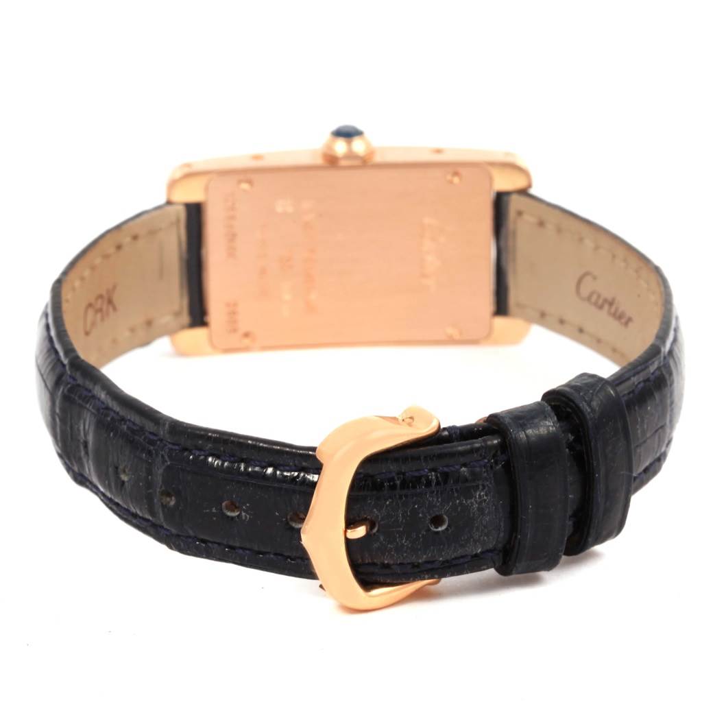 A Cartier Tank Américaine watch is shown from the back, highlighting its case and black leather strap with a gold buckle.