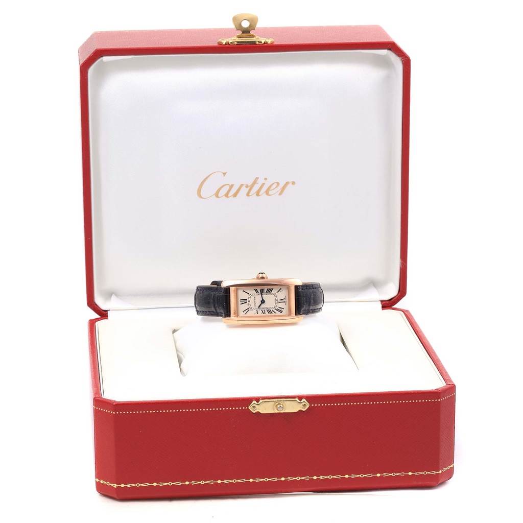 The image shows a Cartier Tank Americaine W2607456 Women
s Rose Gold Silver Dial W2607456 Women
s Rose Gold Silver Dial watch with a black strap and rectangular dial, positioned inside its opened red case.