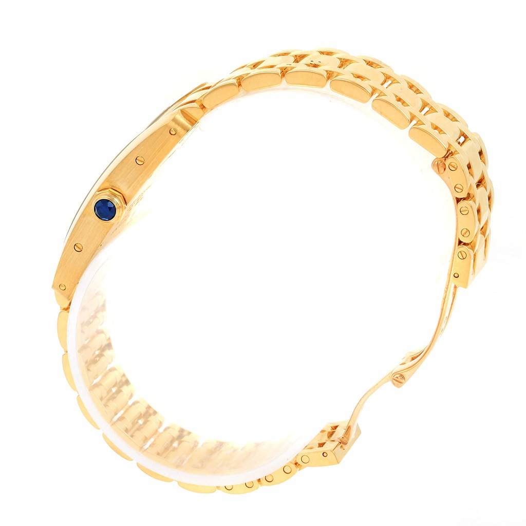 The image shows the side view and bracelet of a Cartier Tank Américaine watch, highlighting its gold finish and crown with a blue gemstone.