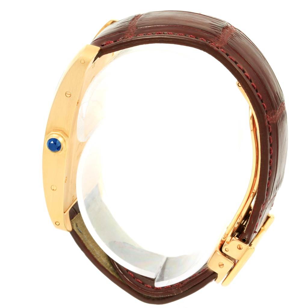 This is a side view of the Cartier Tank Americaine 1735 Men
s Yellow Gold Silver Dial 1735 Men
s Yellow Gold Silver Dial watch, showing its gold casing, crown with blue gemstone, and leather strap.