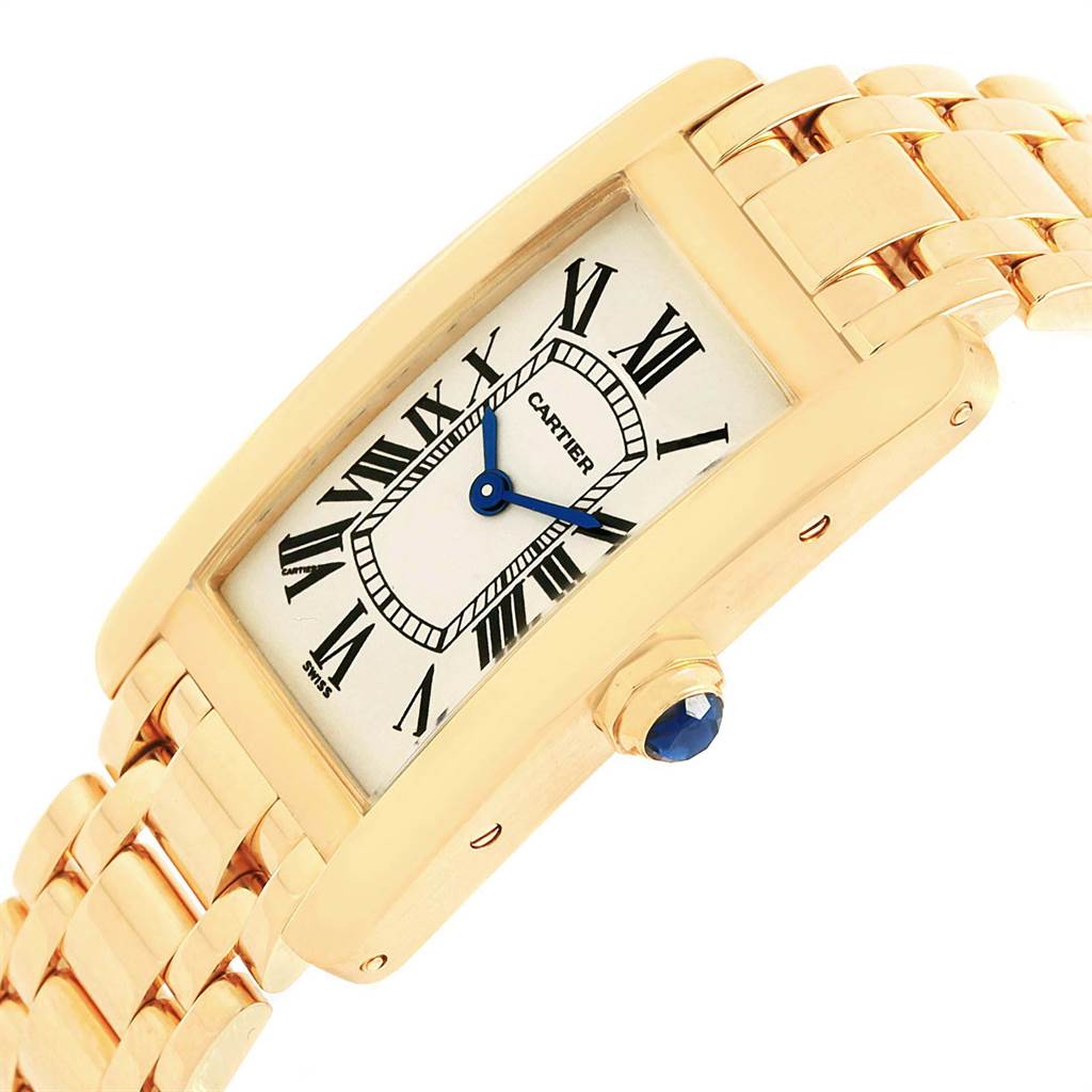The image shows a side angle of the Cartier Tank Americaine W26015K2 Women's Yellow Gold Silver Dial W26015K2 Women's Yellow Gold Silver Dial watch, highlighting its gold bracelet, rectangular face, and blue sapphire crown.