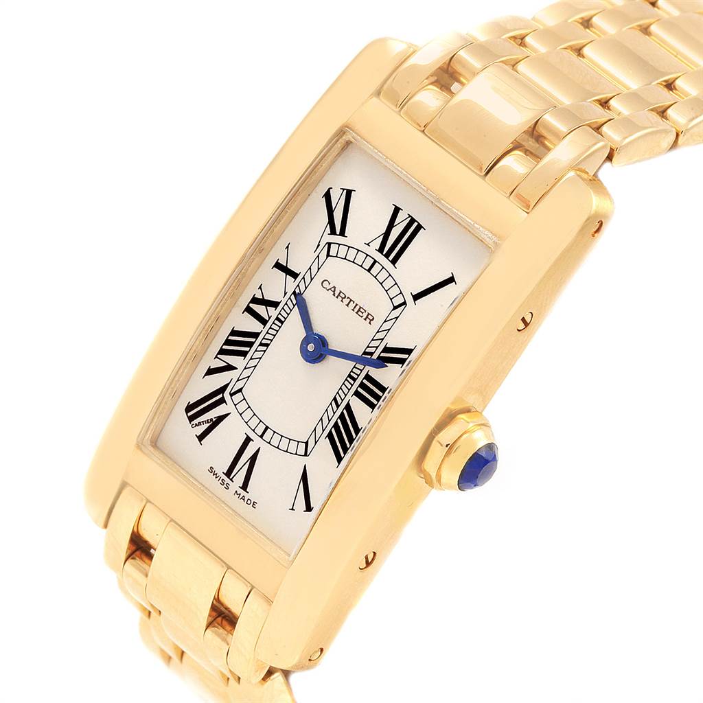 The Cartier Tank Americaine W26015K2 Women's Yellow Gold Silver Dial W26015K2 Women's Yellow Gold Silver Dial watch is shown at an angled view, displaying its gold case, bracelet, dial, and crown with a blue cabochon.